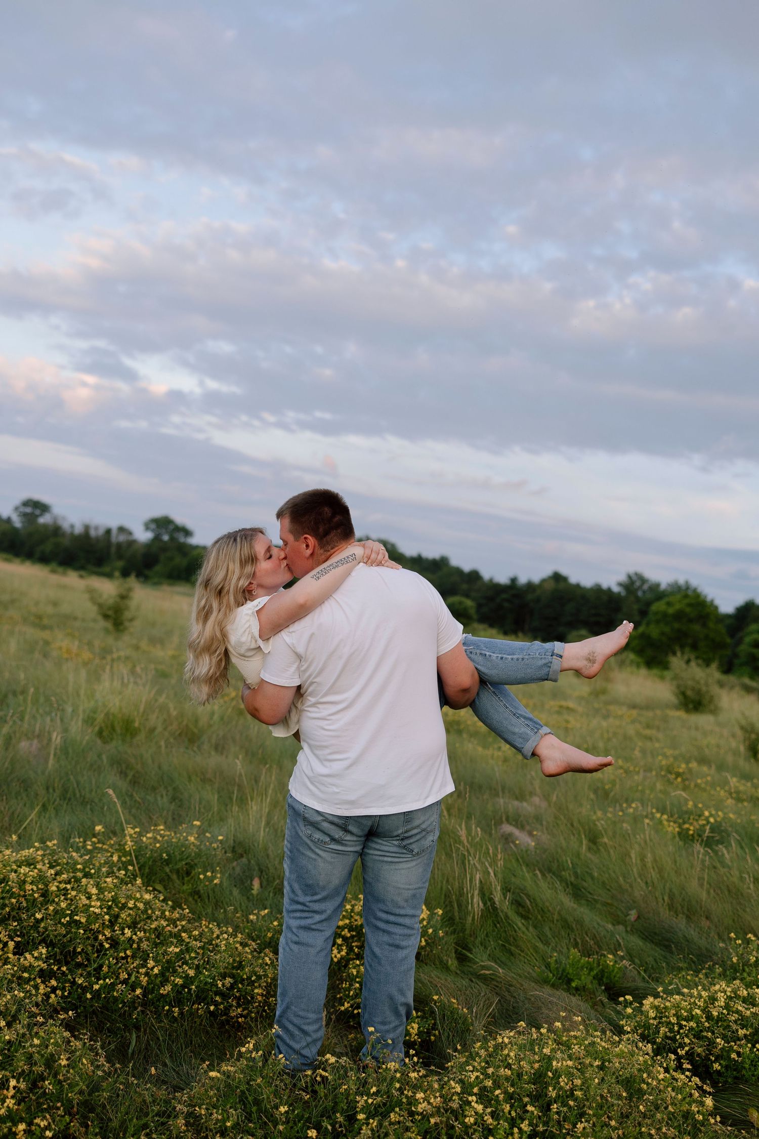 Couple embracing in field of wildflowers during golden sunset at Hamlin Beach State Park for engagement photos.