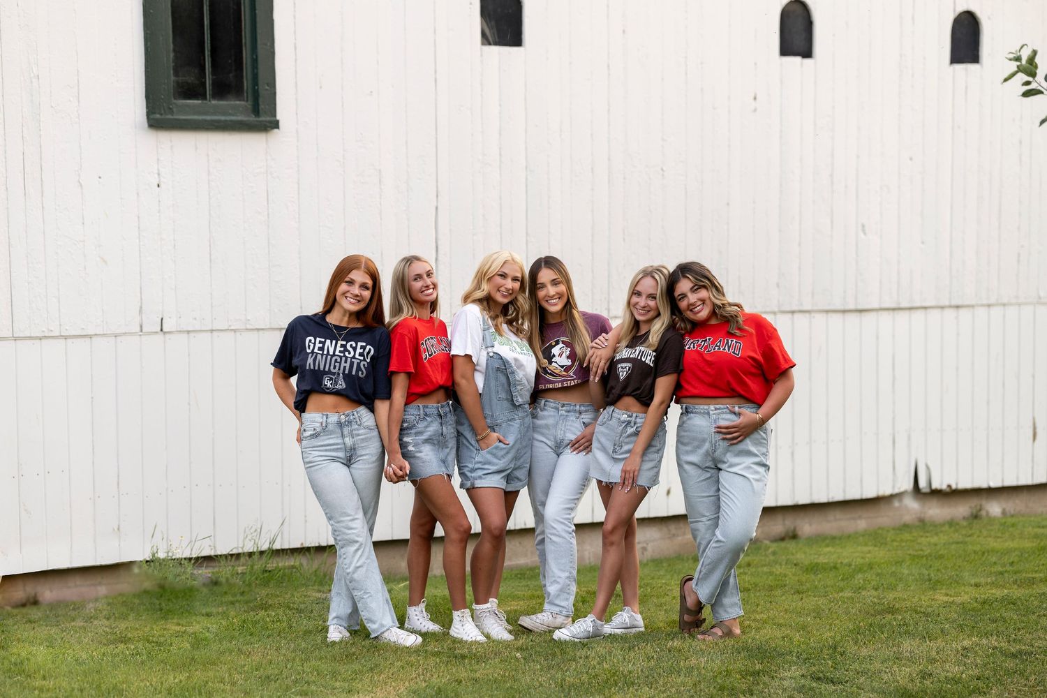 A group of high school graduates wearing their college tshirts against a white barn at Tinker Nature Center for Rochester NY senior portaits