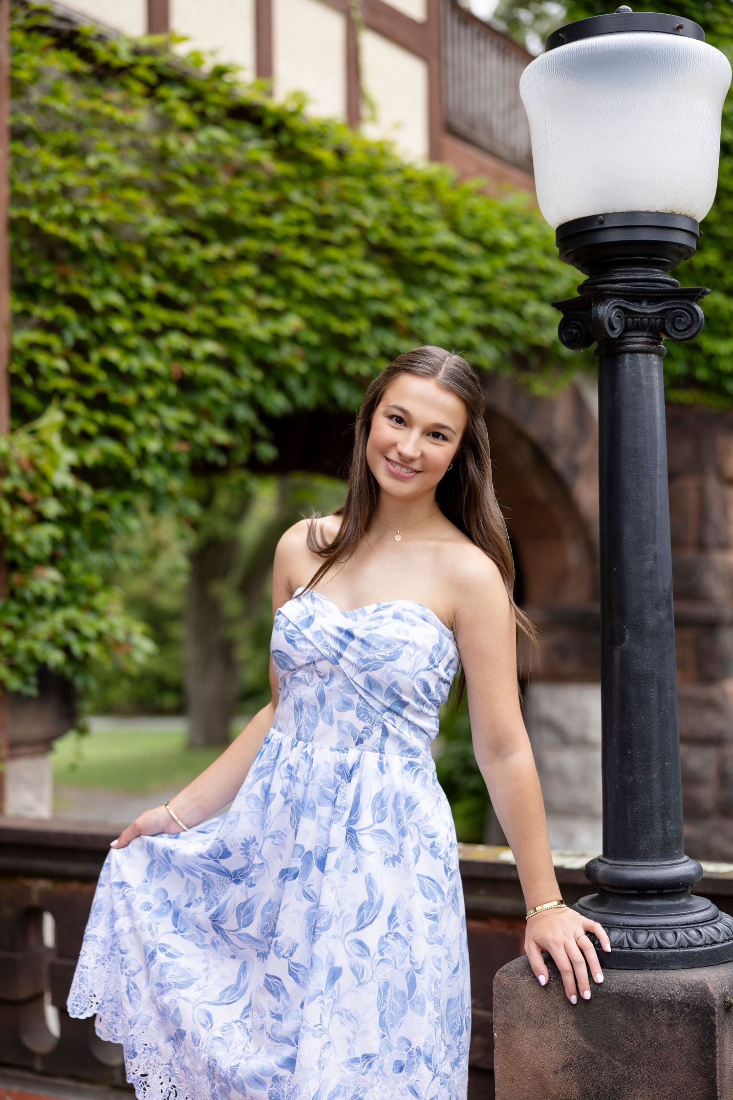 Elegant portrait with blue and white floral dress against vintage lamp post and ivy wall at Sonnenburg Mansion and Gardens.