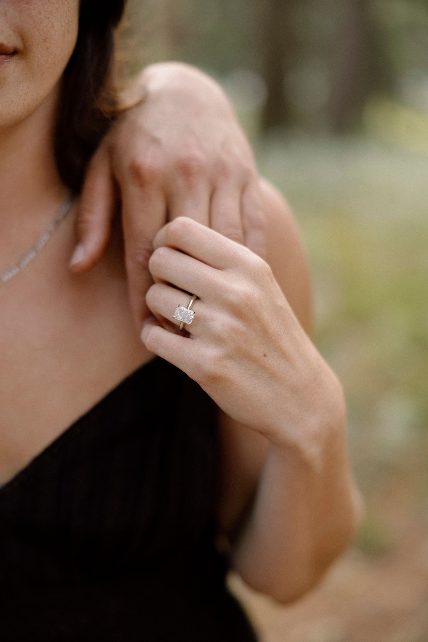 Close-up shot of an engagement ring on a hand against a dark background.