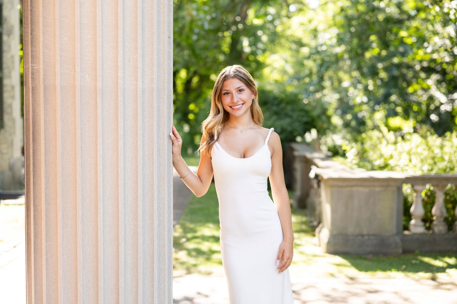 Senior portait at classical stone columns create an elegant architectural backdrop in a sunlit George Eastman House and garden setting.