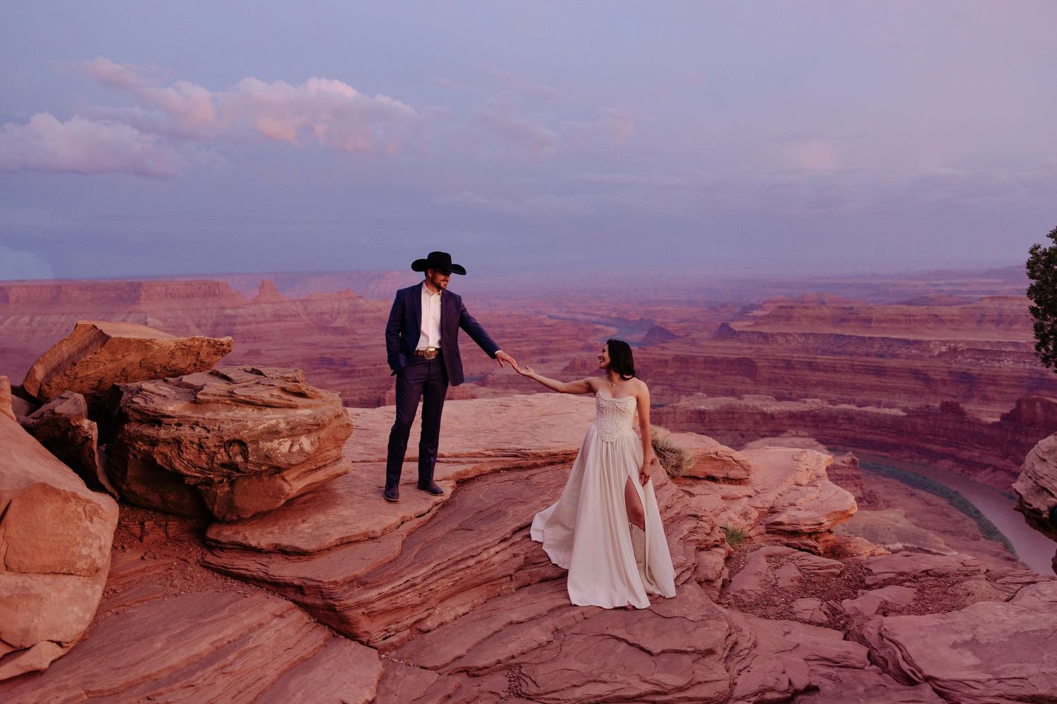 A wedding couple poses on dramatic red rock formations in a desert landscape in Moab Utah for elopement photoshoot.