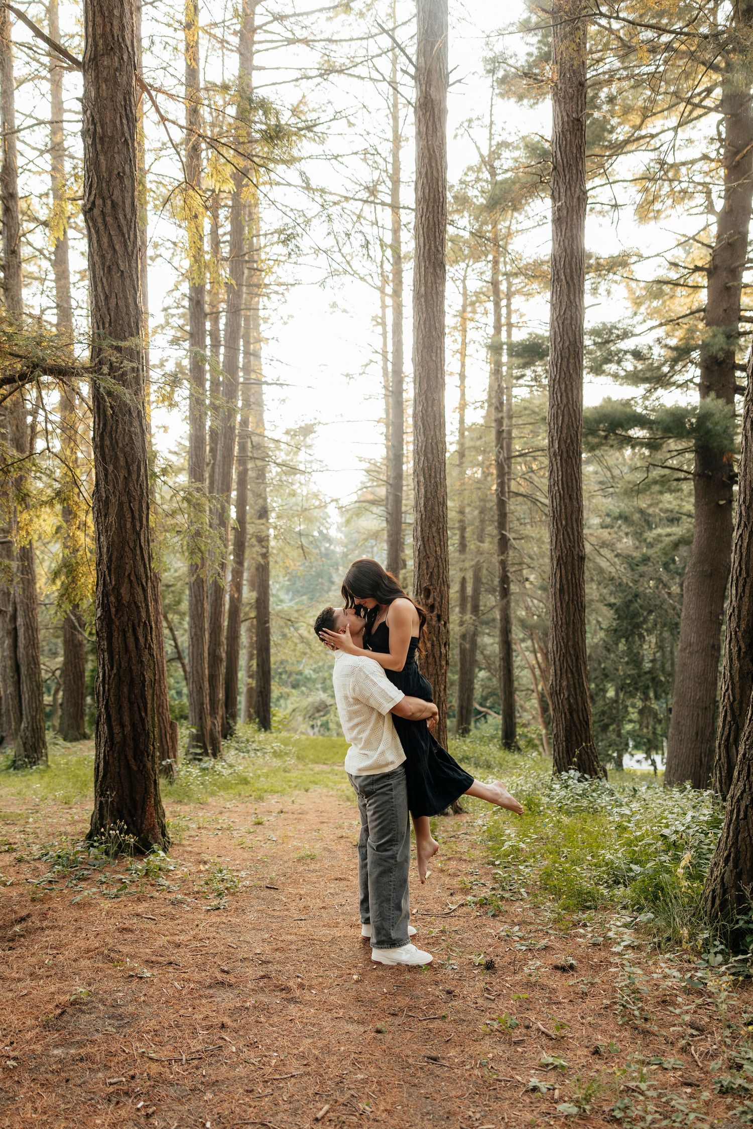 Playful couple enjoys a romantic moment in a golden sunlit forest setting at Highland Park
