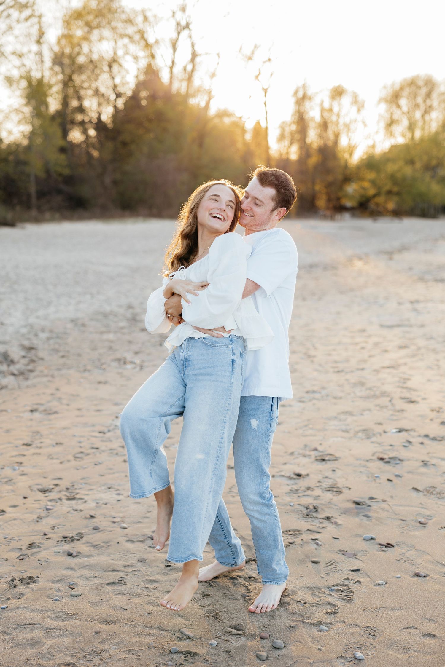 A playful couple in casual attire sharing intimate moments on a sandy Durand beach at sunset for Rochester Engagement photos.