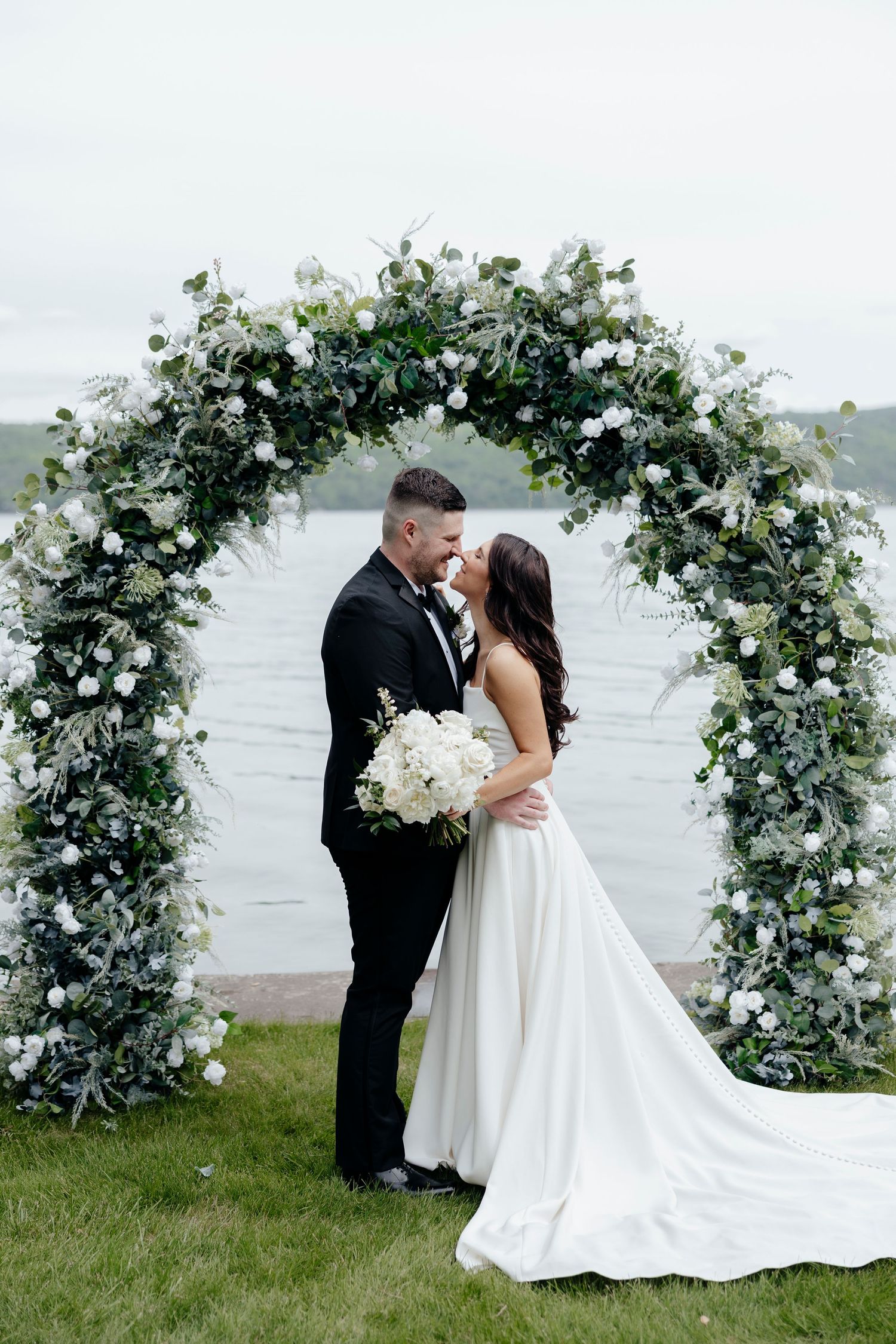 Elegant wedding ceremony setup with white floral arch overlooking water at Canandaigua Lake.