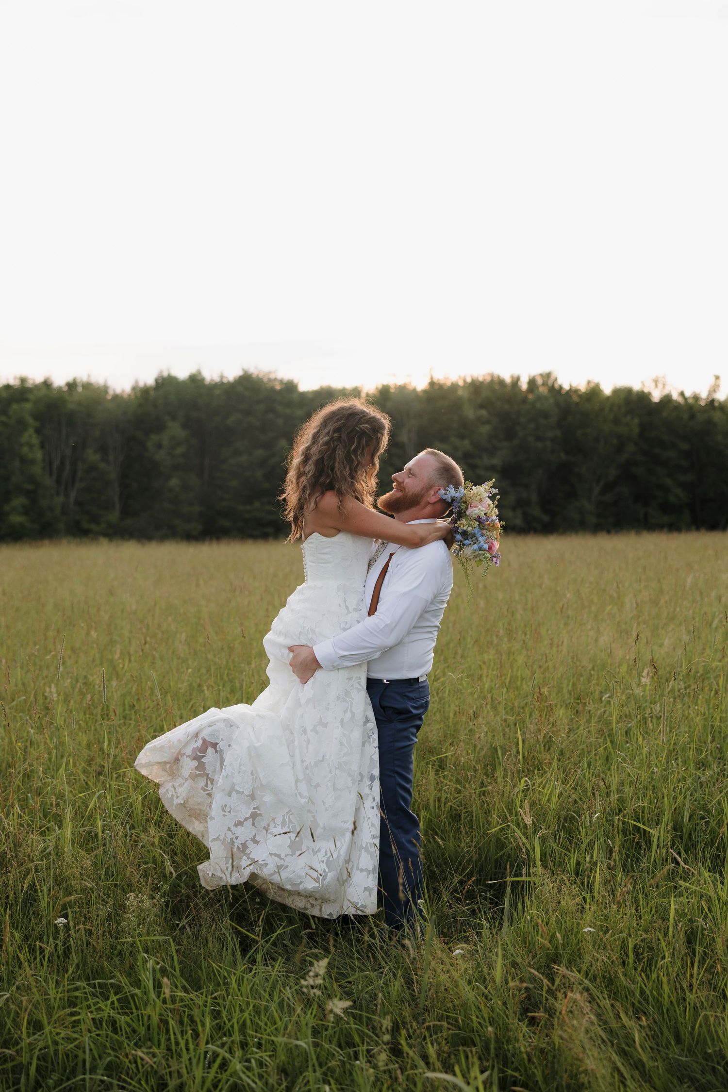 Couple embraces in tall grass field during golden hour wedding photoshoot in Rochester, NY