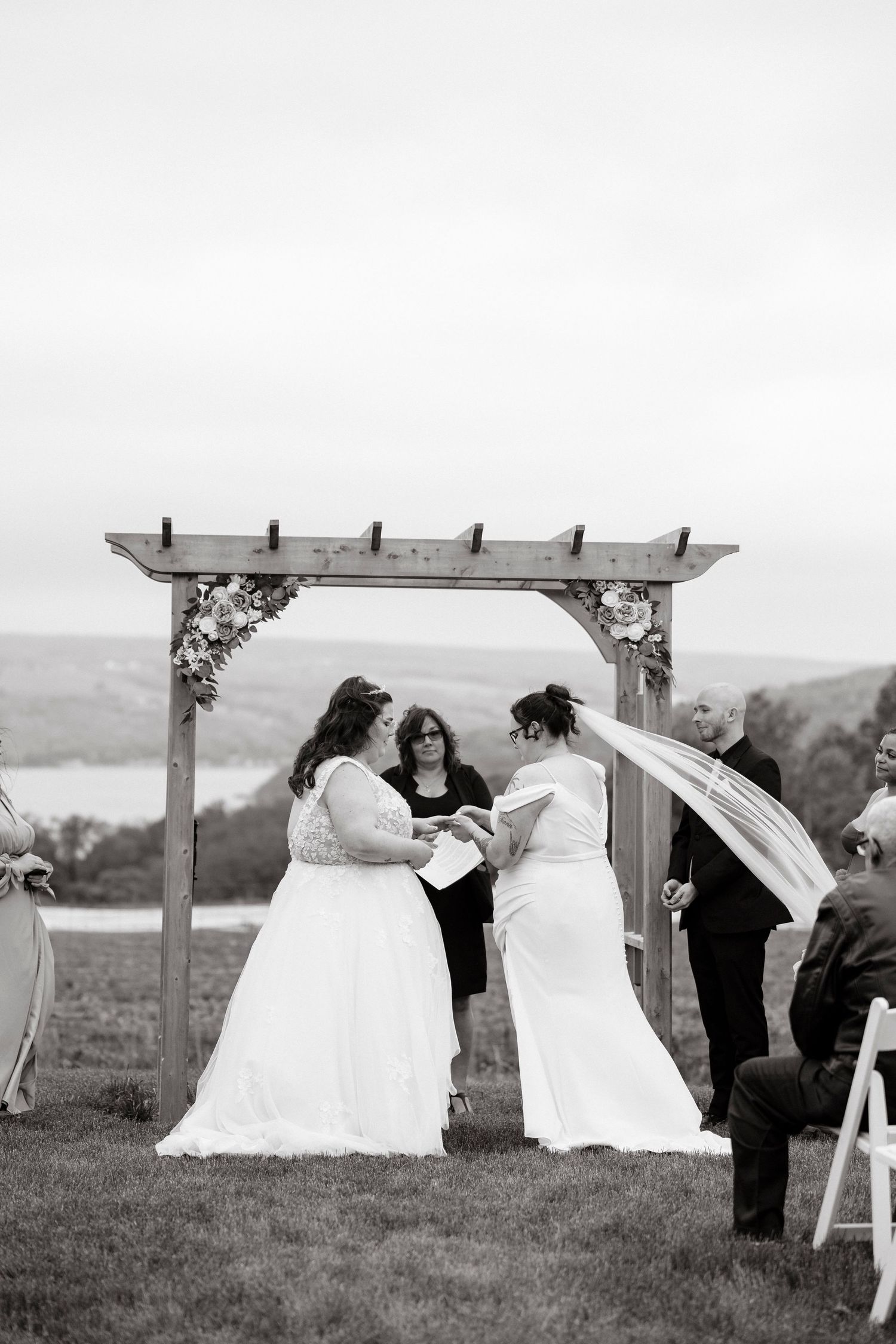 Black and white photo of two brides in wedding dresses saying their vows at the alter overlooking Keuka NY during Winery wedding day.