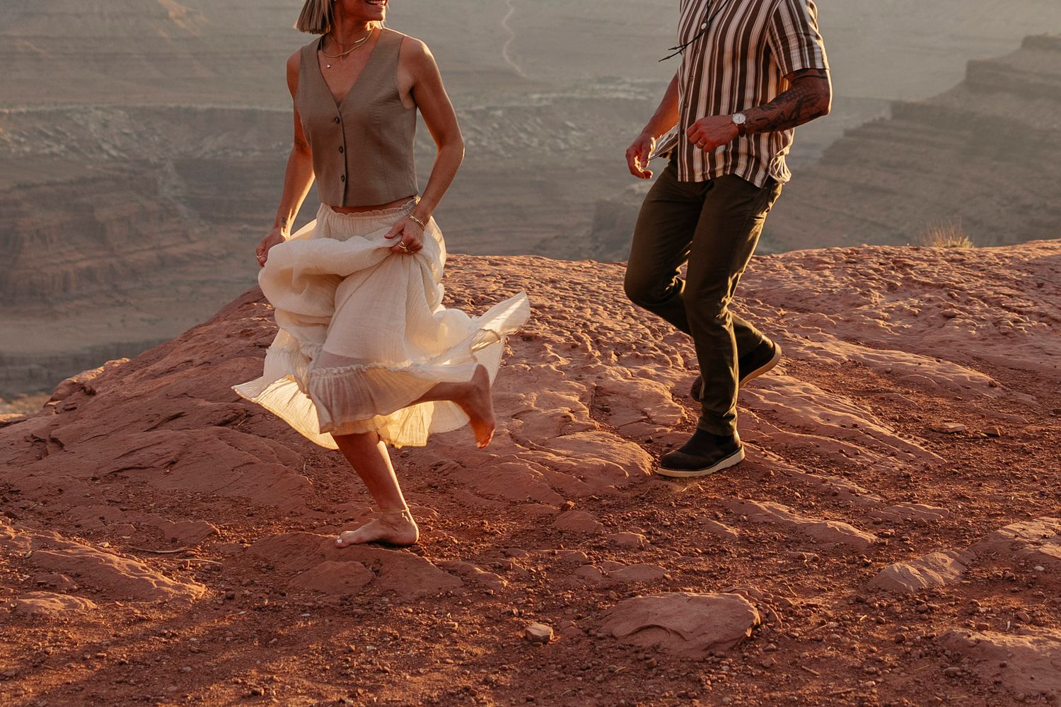 Couple walking along a red rock cliff edge at sunset at Dead Horser State Park