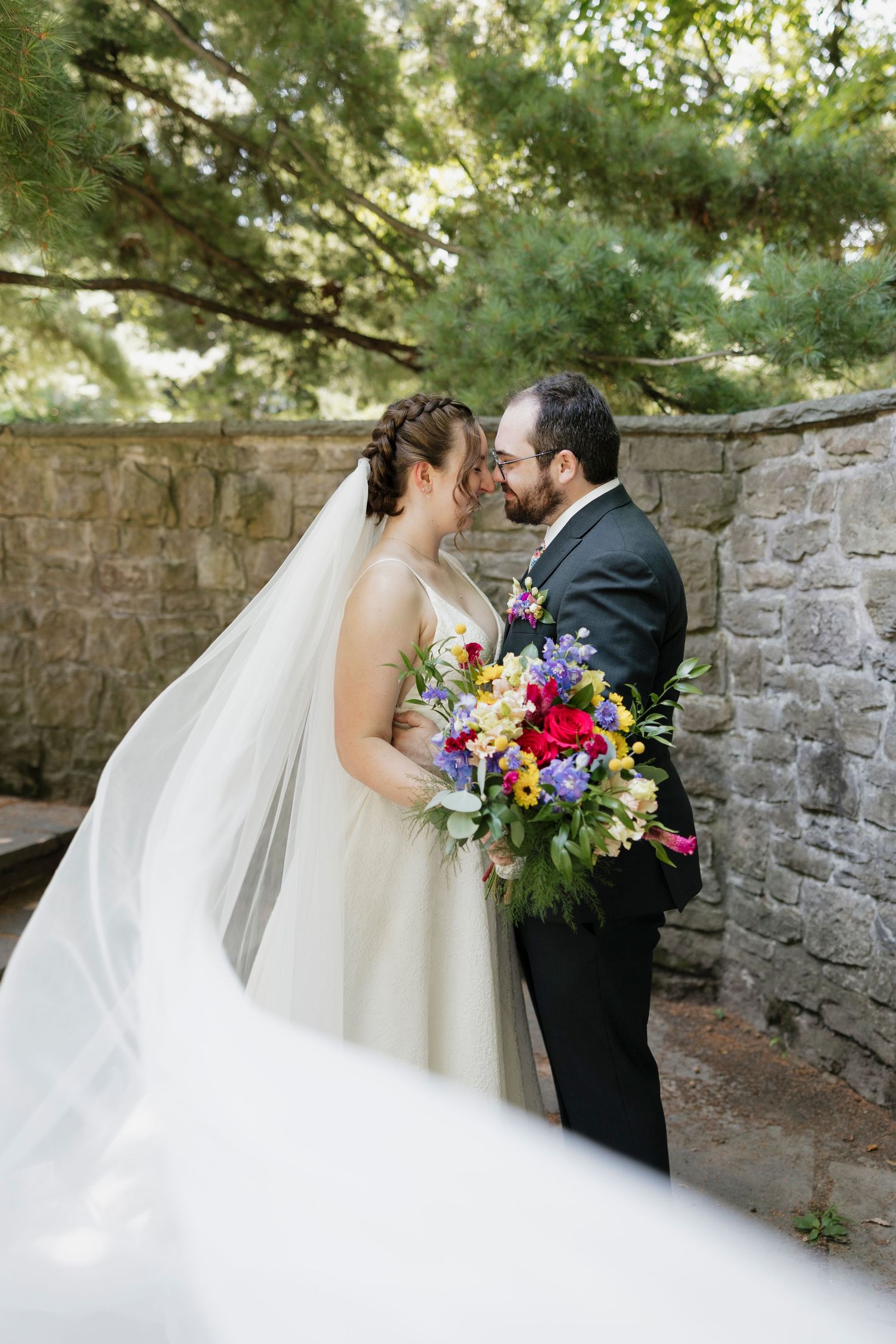 Romantic wedding portrait against stone wall with flowing white dress and colorful bouquet, Sunken Garden bridal portaits Rochester, NY.