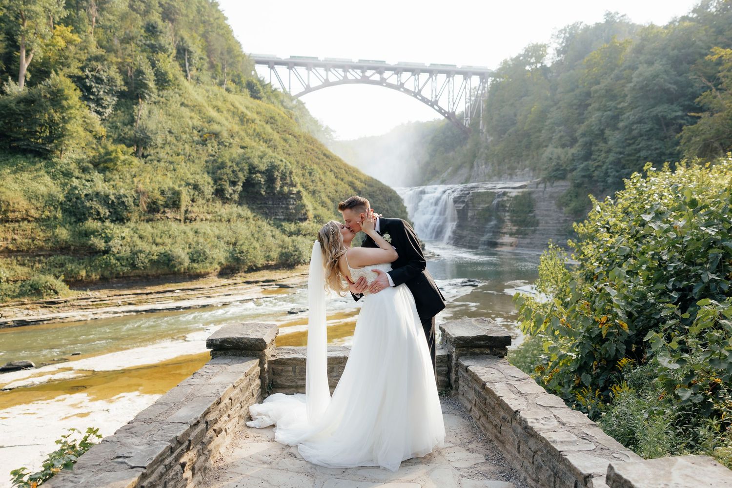 Wedding photos taken at a scenic gorge location with a bridge and waterfall in the background at Letchworth NY elopement.