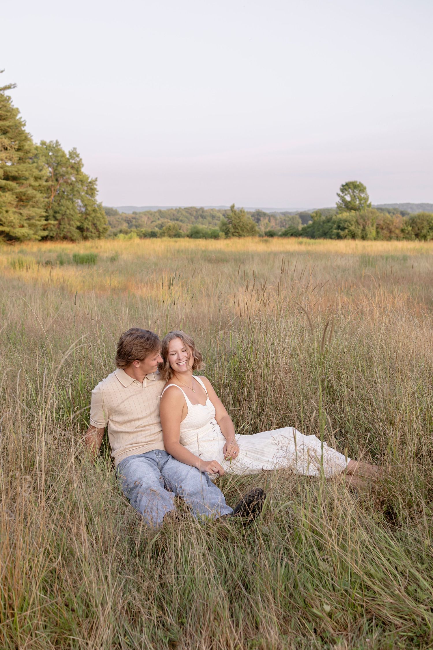 A couple relaxes in a tall grass field during golden hour at Knox Farm State Park in Buffalo, NY.
