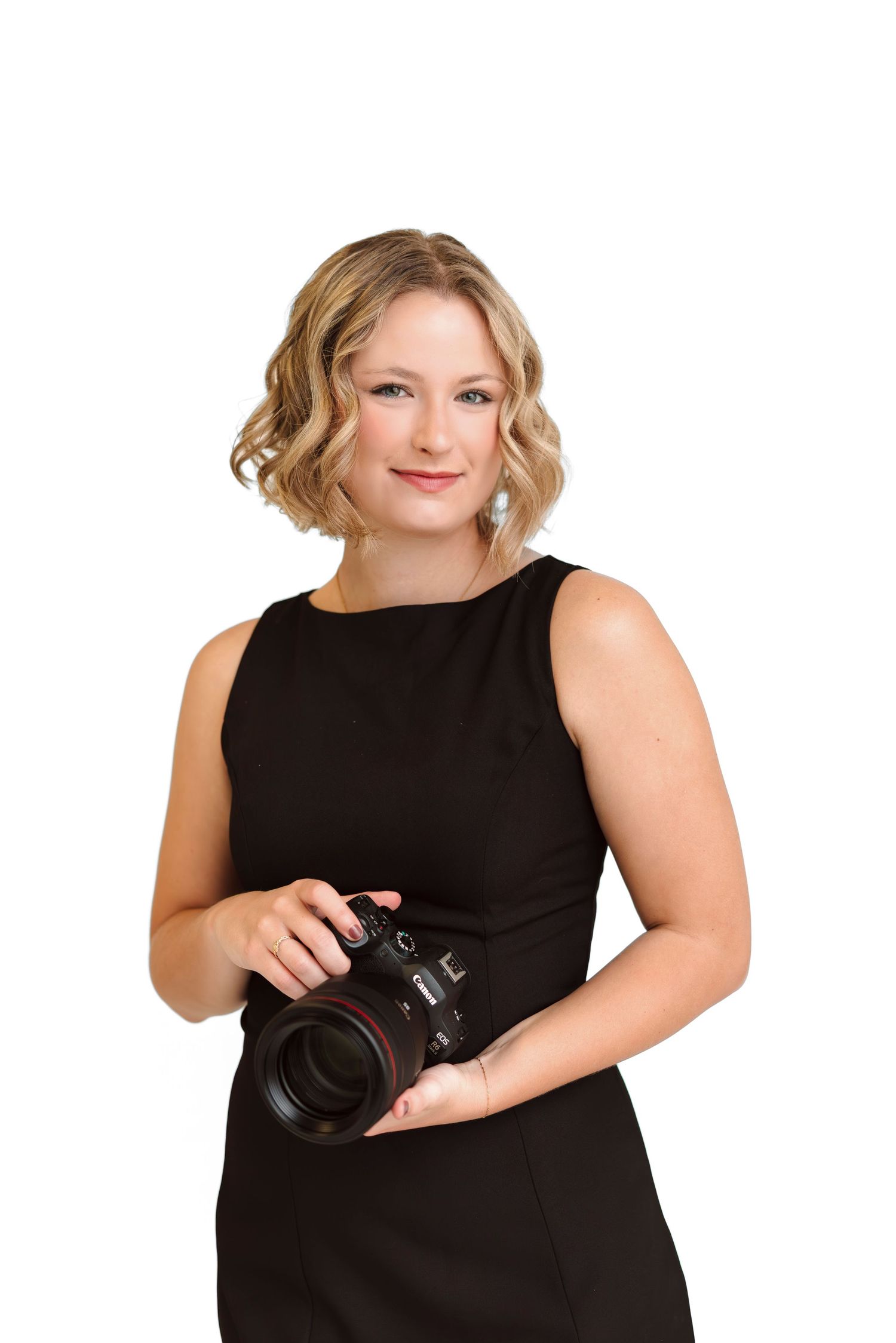 Professional photographer in black sleeveless top poses with DSLR camera against white background in studio setting.