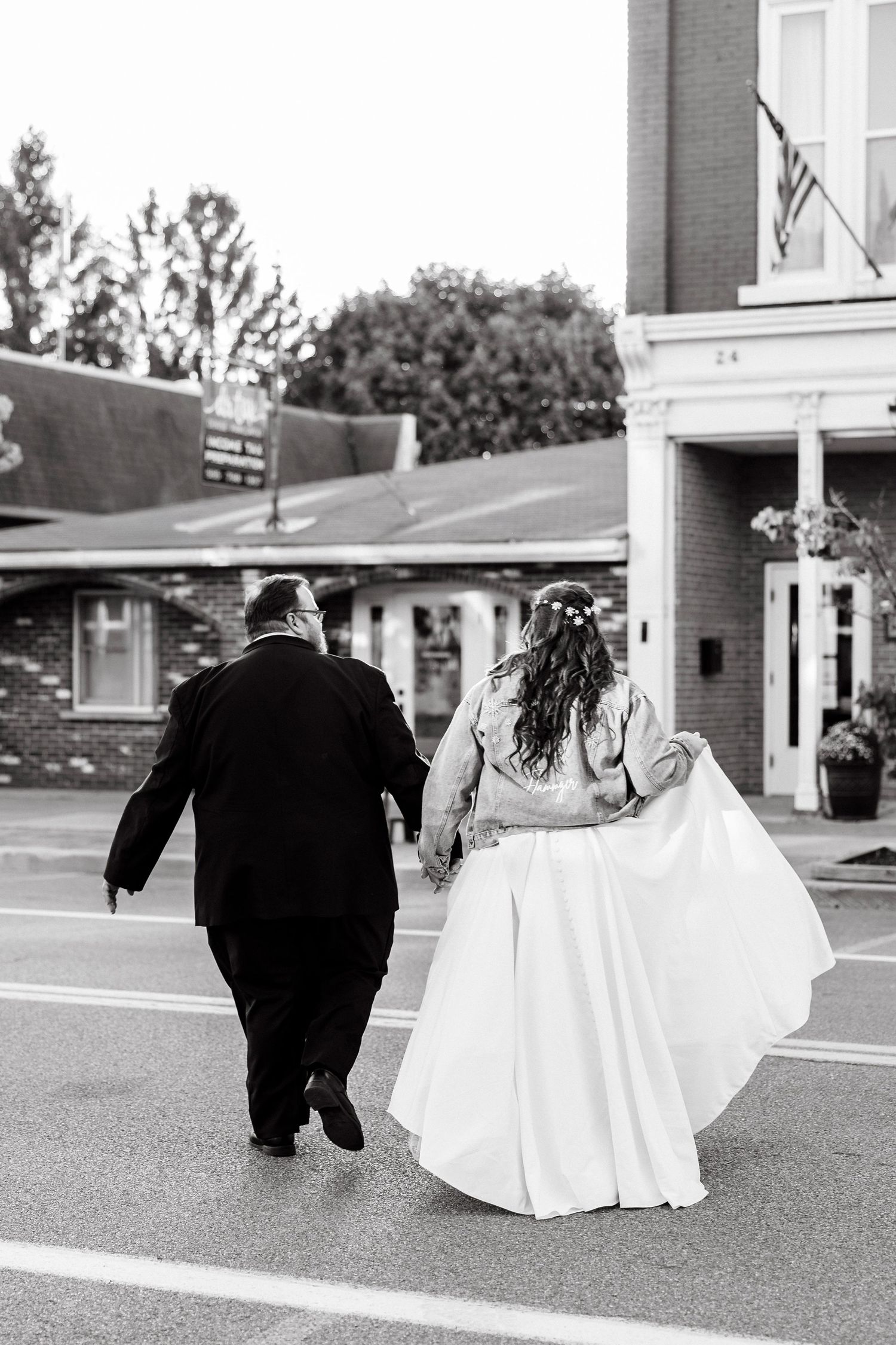 A couple in wedding attire walking together down a street in black and white in Middleport, NY