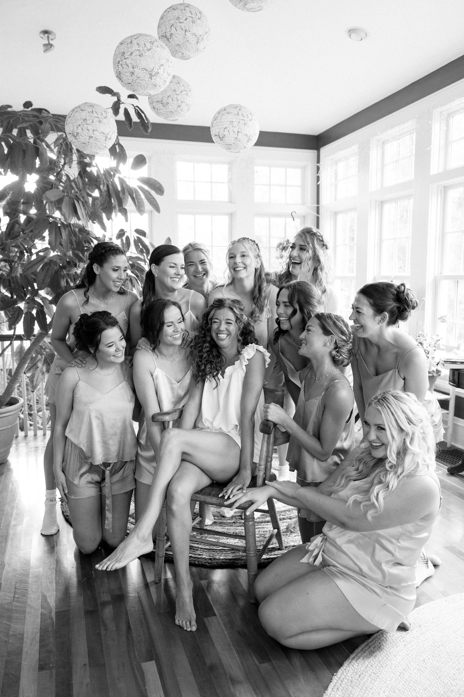 Black and white photo of a group of bridesmaids in matching robes share laughter and joy during pre-wedding preparations.