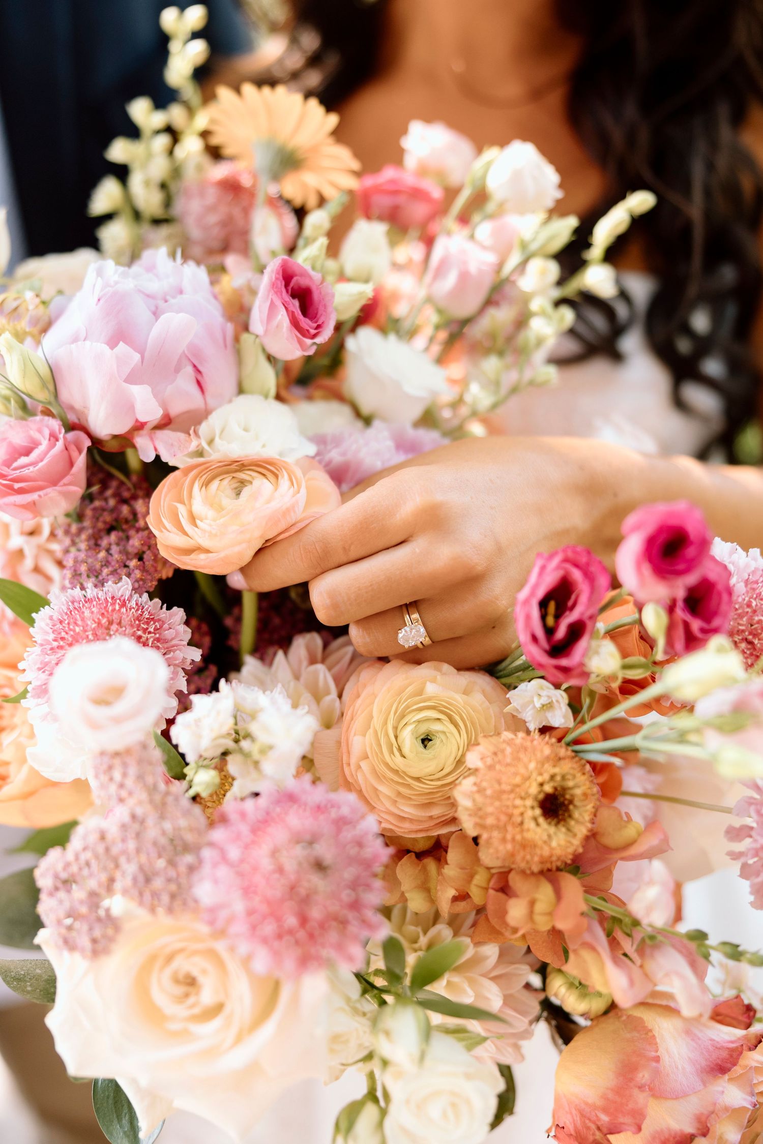 Elegant arrangement of pink and peach flowers including roses and ranunculus in soft natural light for sunrise colored wedding bouquet.