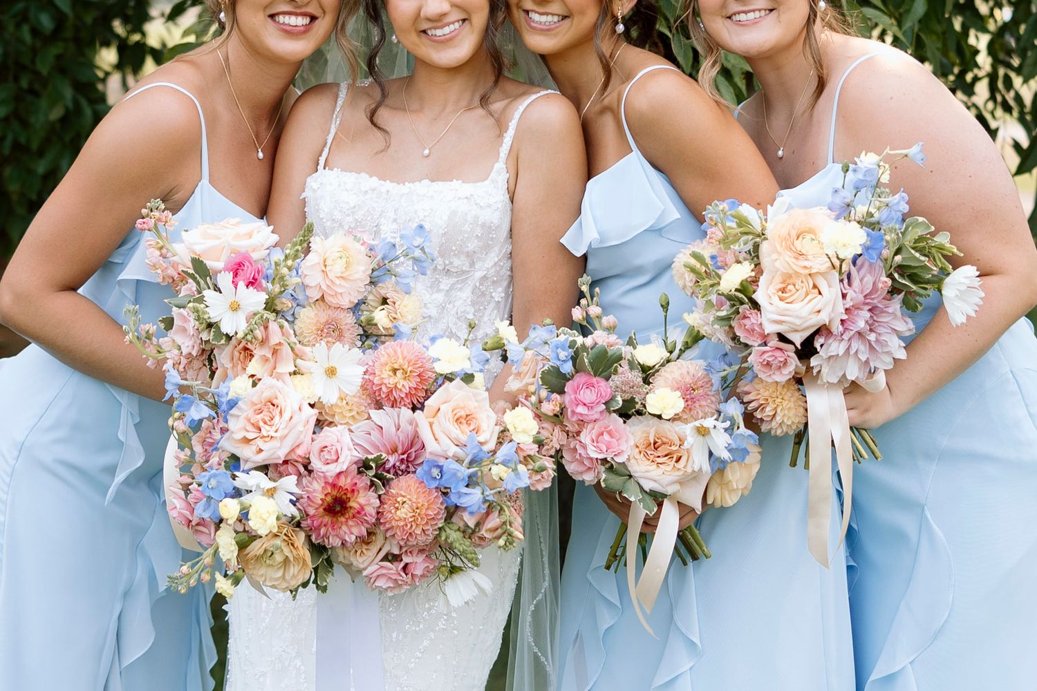 Bridal party in light blue dresses holding pastel bouquets with roses and delphinium flowers at Shadow Lake Wedding