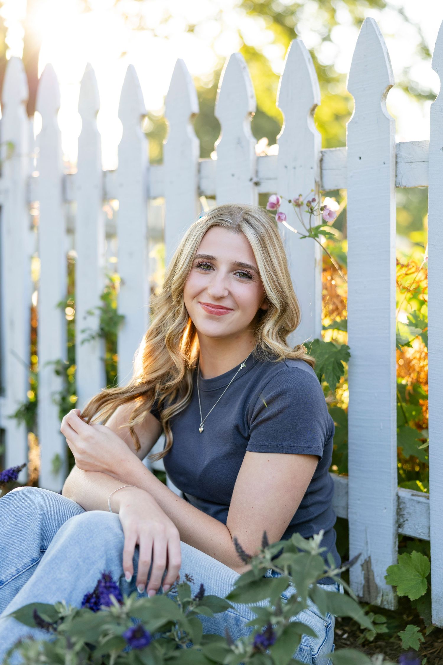 Portrait against white picket fence with flowers and greenery in background at Webster Arboretum for Rochester NY senior portaits.