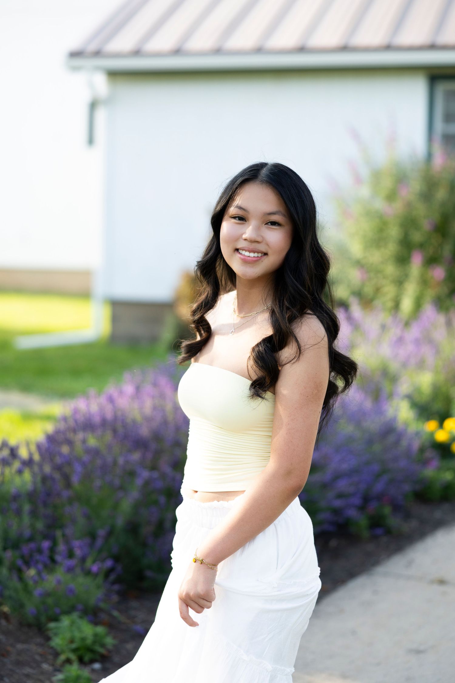 Summer portrait in yellow top and white skirt with purple flowers in background at Tinker Nature Center in July. Rochester senior portaits.