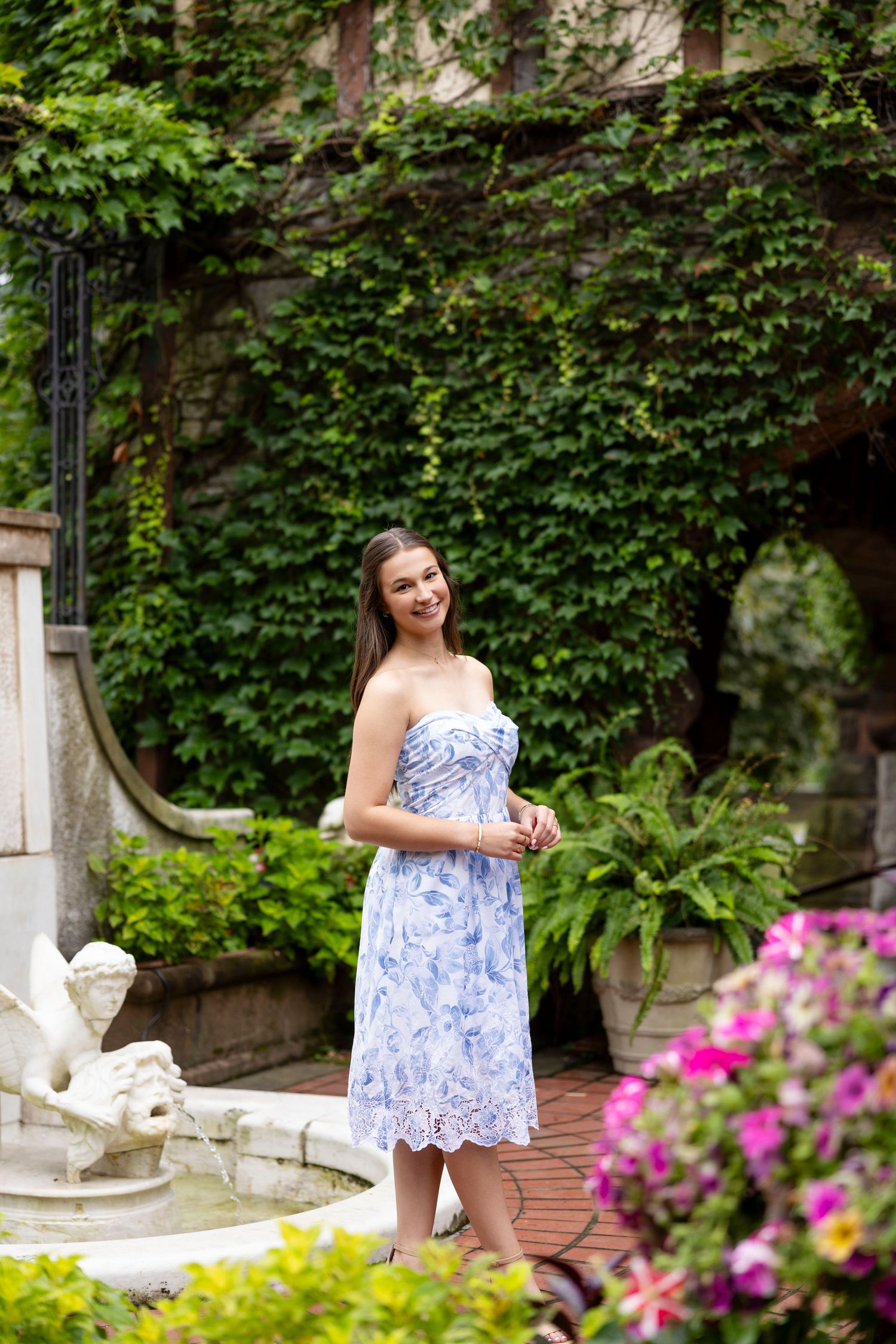 A portrait session in a blue and white dress among ivy-covered garden walls and pink flowers at Sonnenburg Mansion Rochester NY senior photo