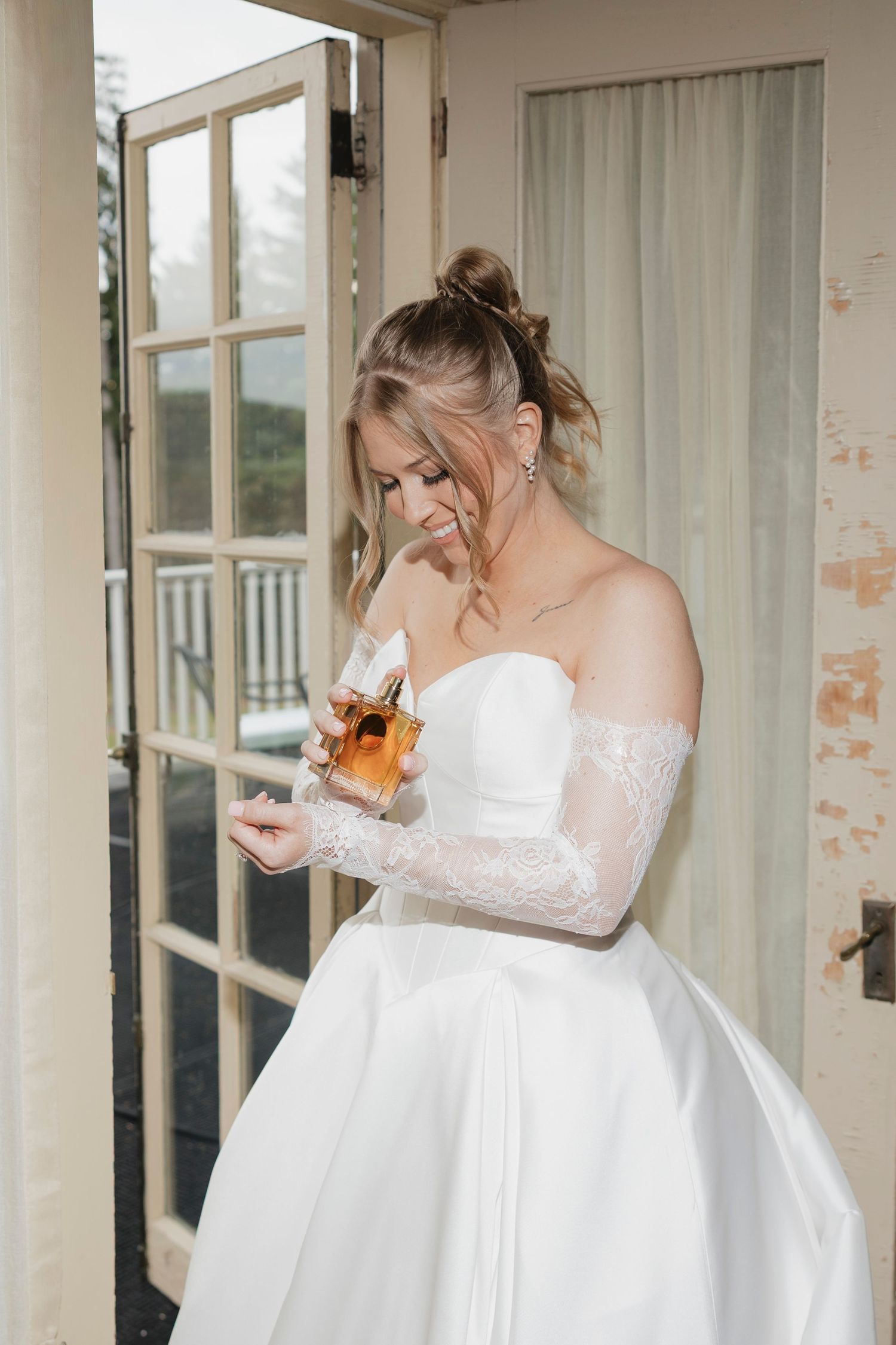 Bride in classic white ballgown with lace sleeves sprays on perfume on her balcony before walking down the aisle in Rochester, NY.