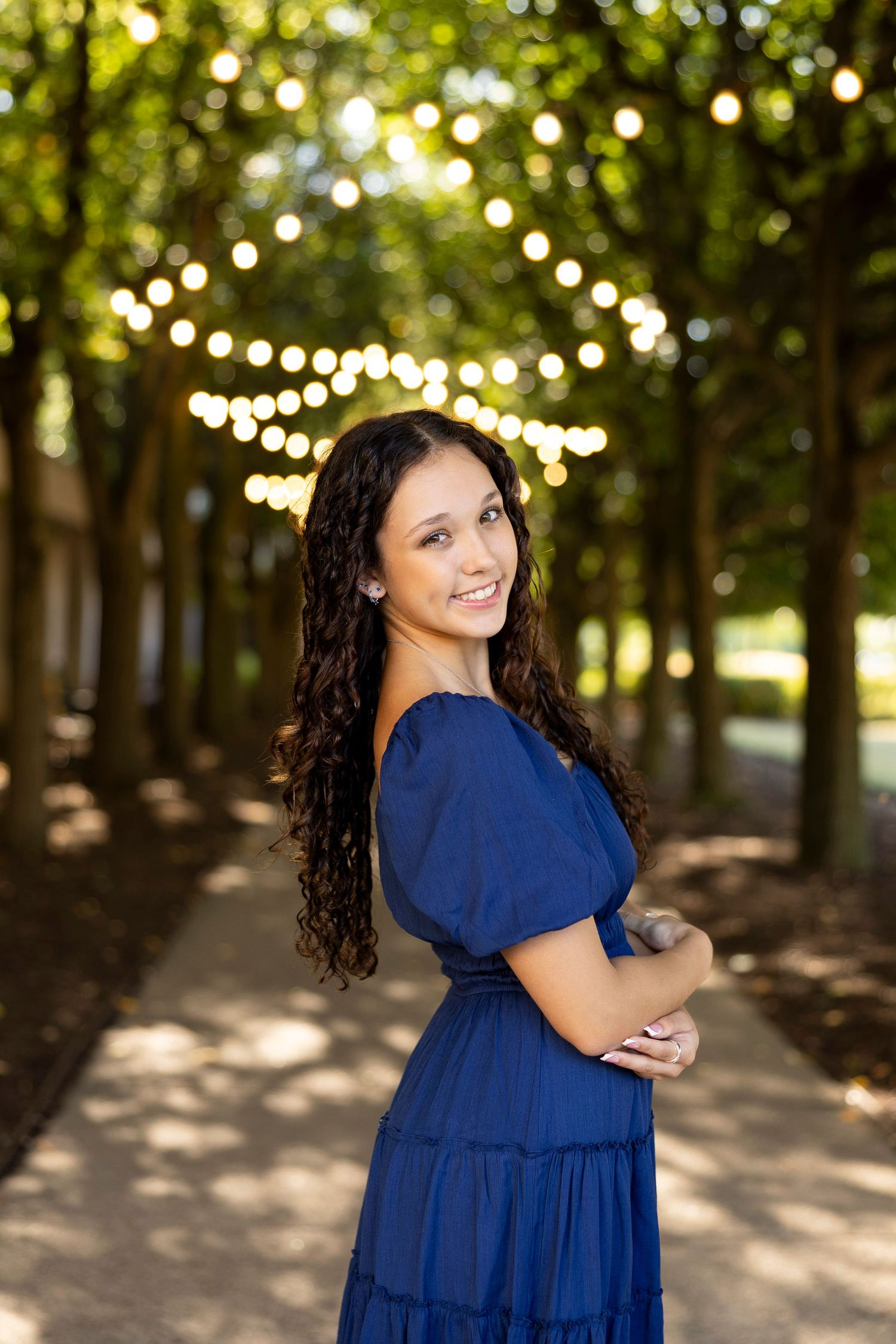 Senior portrait session under twinkling string lights in a tree-lined path with navy blue dress at the Memorial Art Gallery, Rochester, NY.