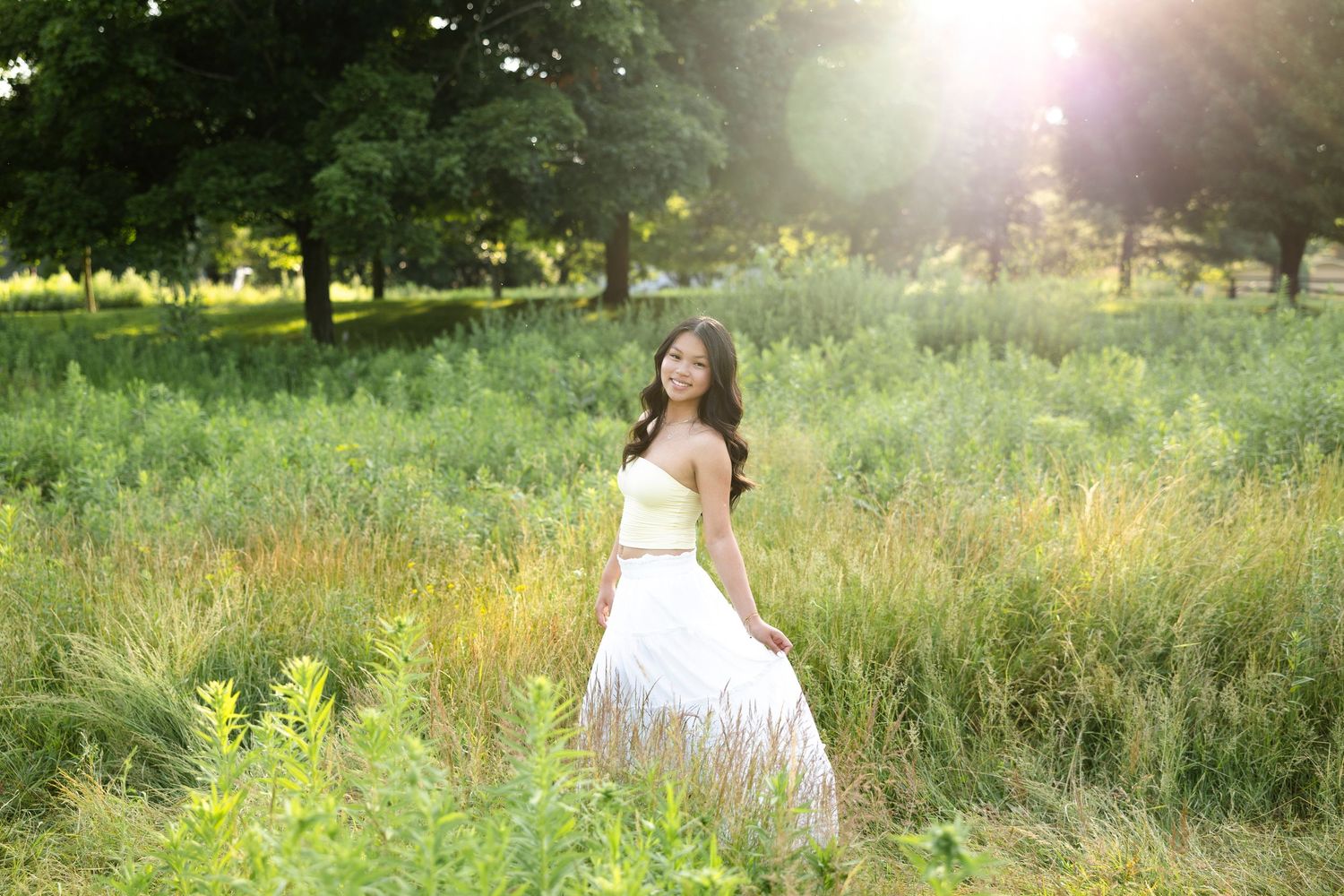 Senior portait wearing dress in sunlit meadow with wildflowers and tall grass during golden hour at Tinker Nature Center, Rochester, NY.