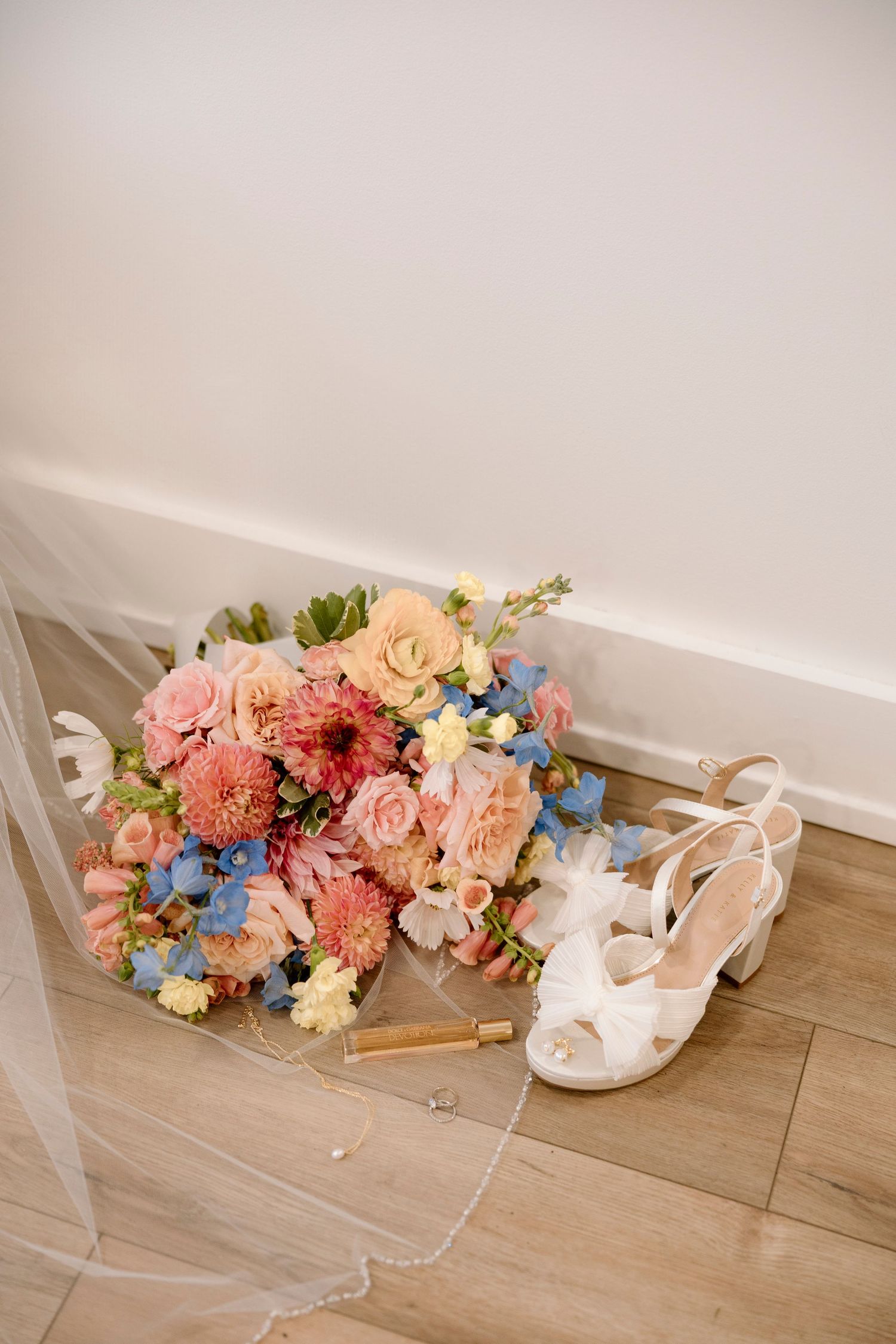 Wedding accessories including white shoes, a veil, and colorful floral bouquet arranged on wooden flooring at Shadow Lake wedding.