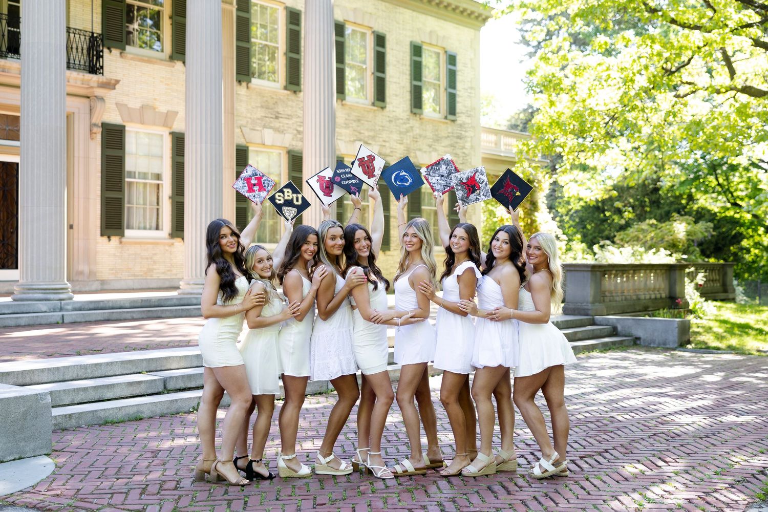 Graduation photo series with people in white dresses posing by classical architecture columns holding up their grad caps.