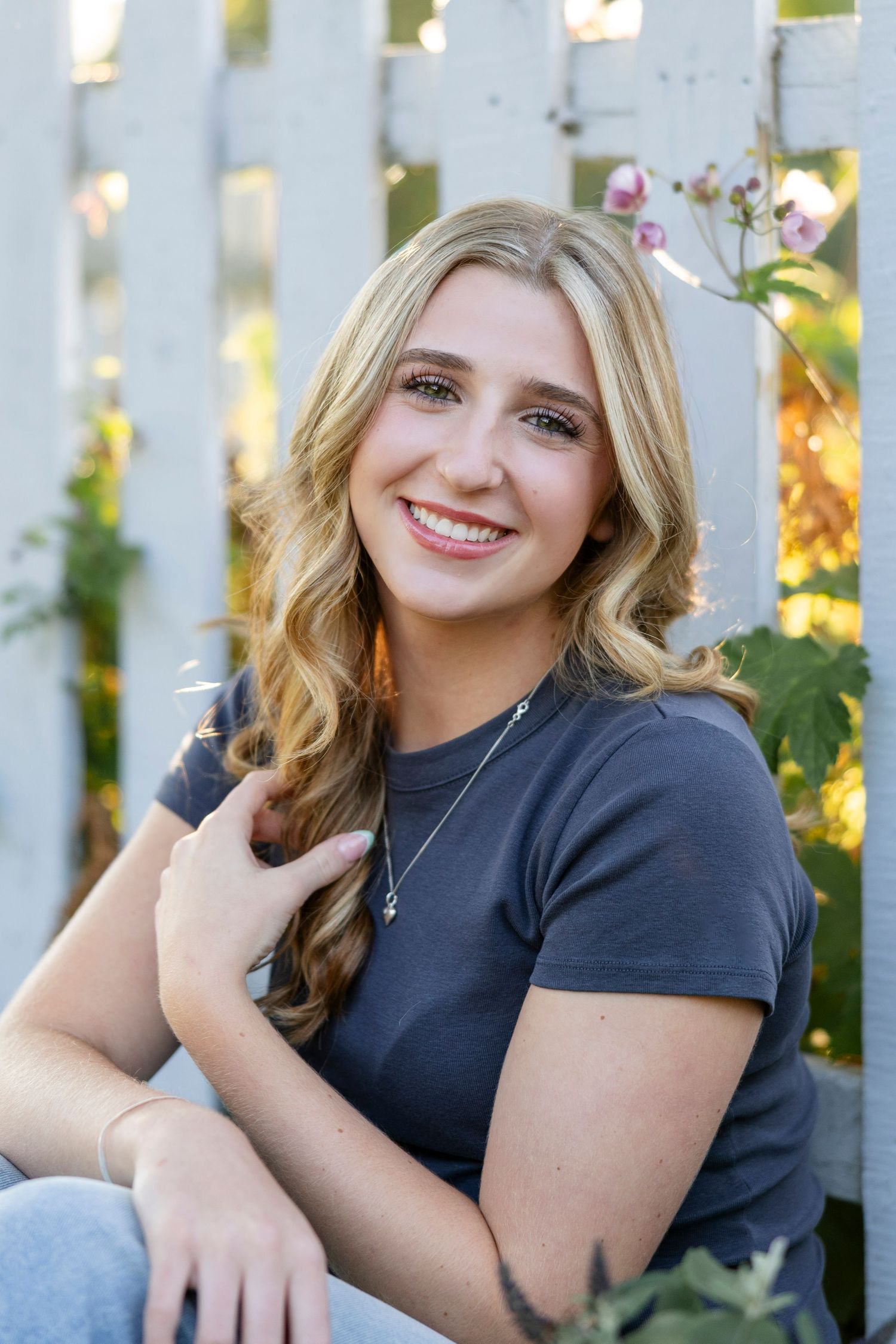 High School senior portrait session against white picket fence in natural lighting at Webster Arboretum. Senior photos in Rochester, NY.