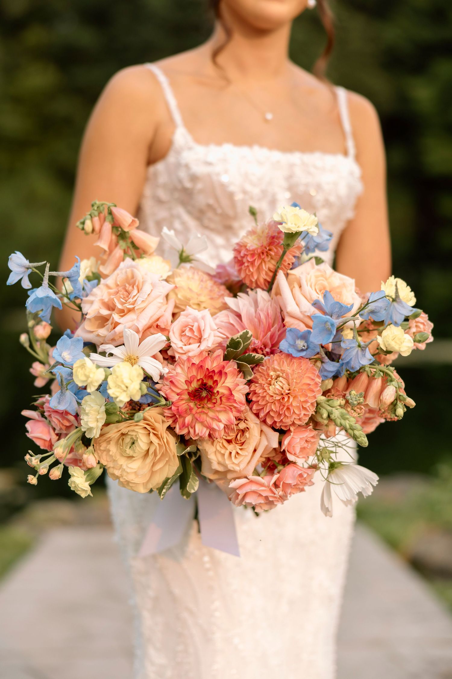 Colorful bridal bouquet featuring pink carnations, blue delphiniums, and peach roses in a romantic garden style. Rochester NY Garden Wedding