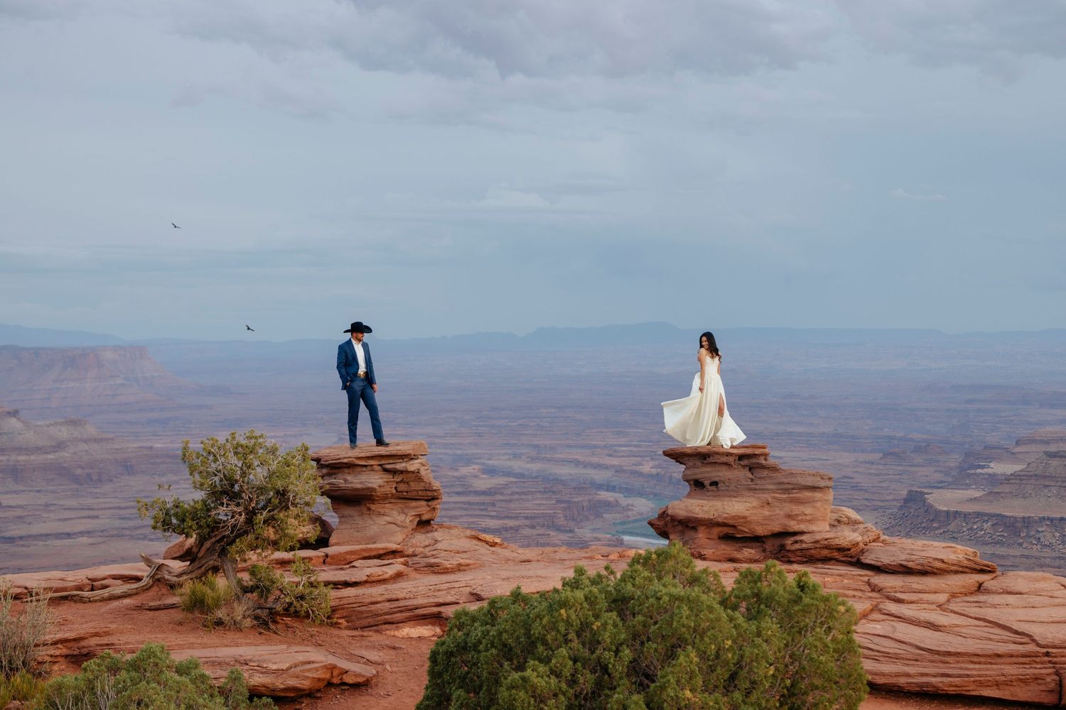 Dramatic wedding photos on red rock cliffs overlooking vast desert canyon landscape in Moab, Utah for elopement.