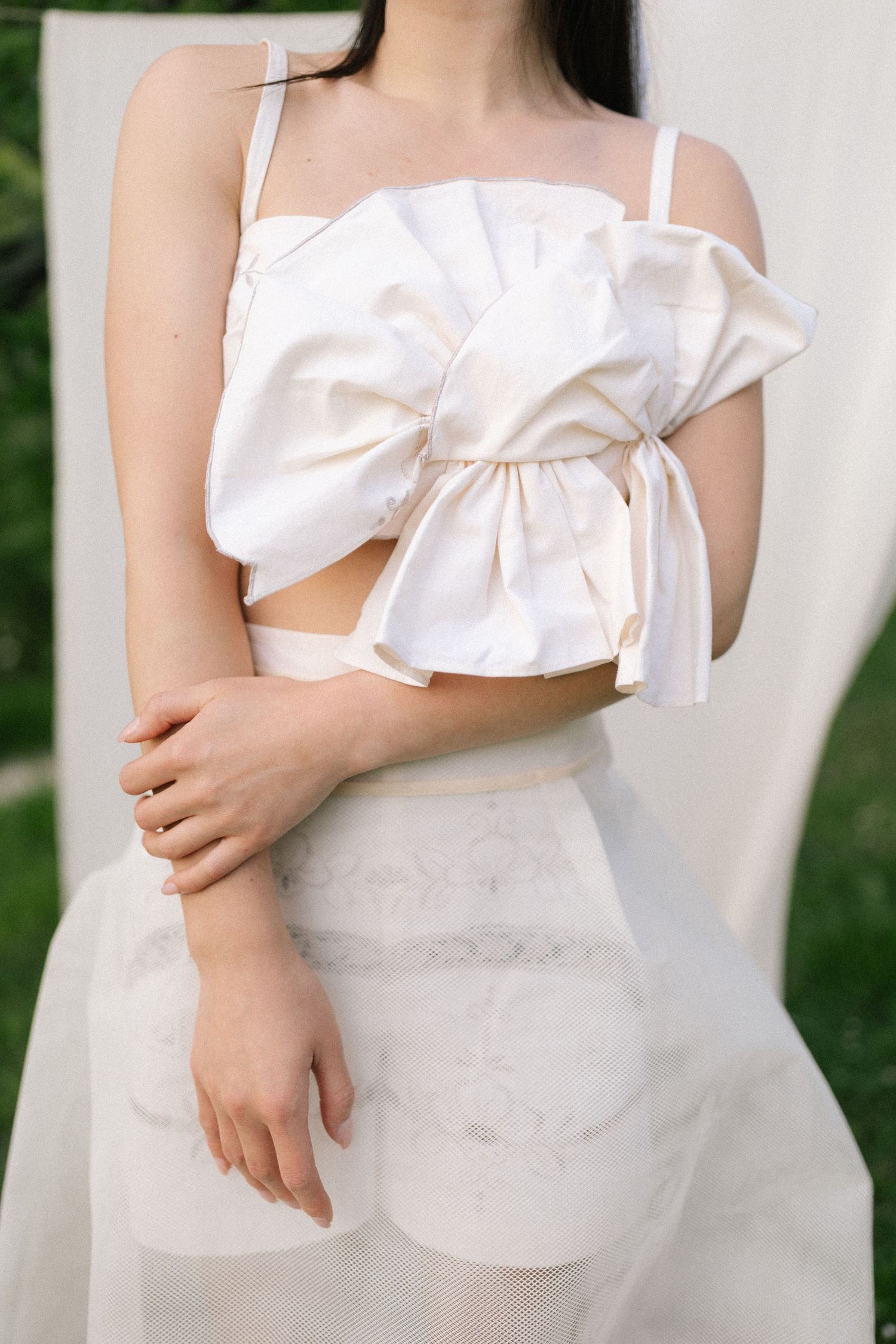 Woman wearing a white ruffled crop top with bow detail and sheer white skirt in an outdoor setting.