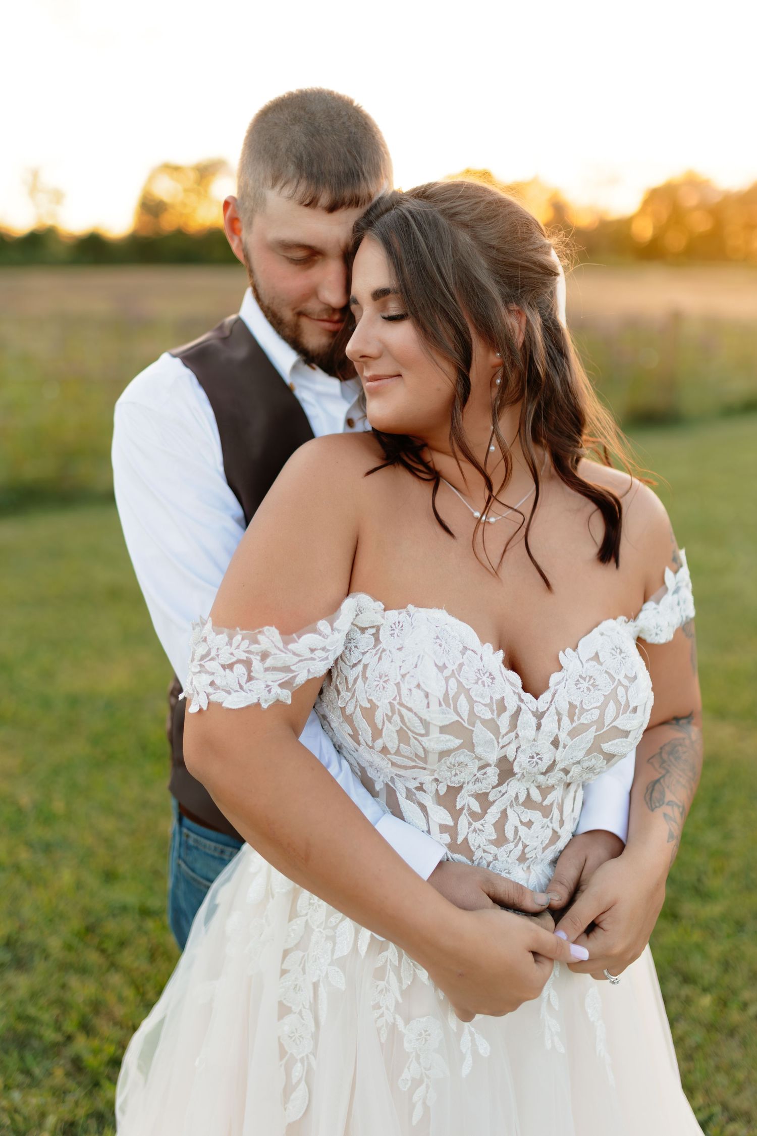 Intimate wedding couple portraits at sunset in a grassy field showing tender embraces.