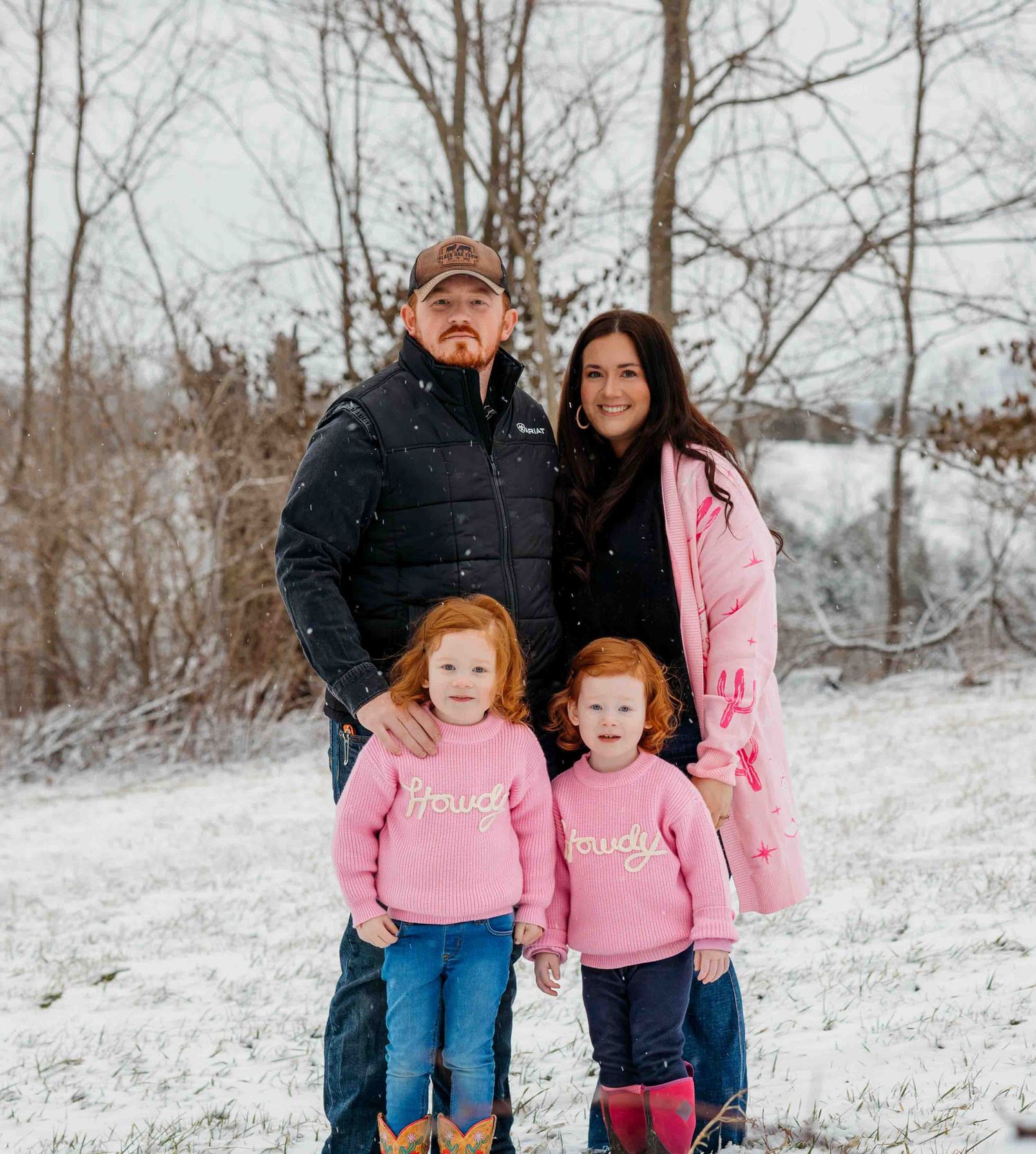 A winter family portrait in the snow with matching pink outfits.