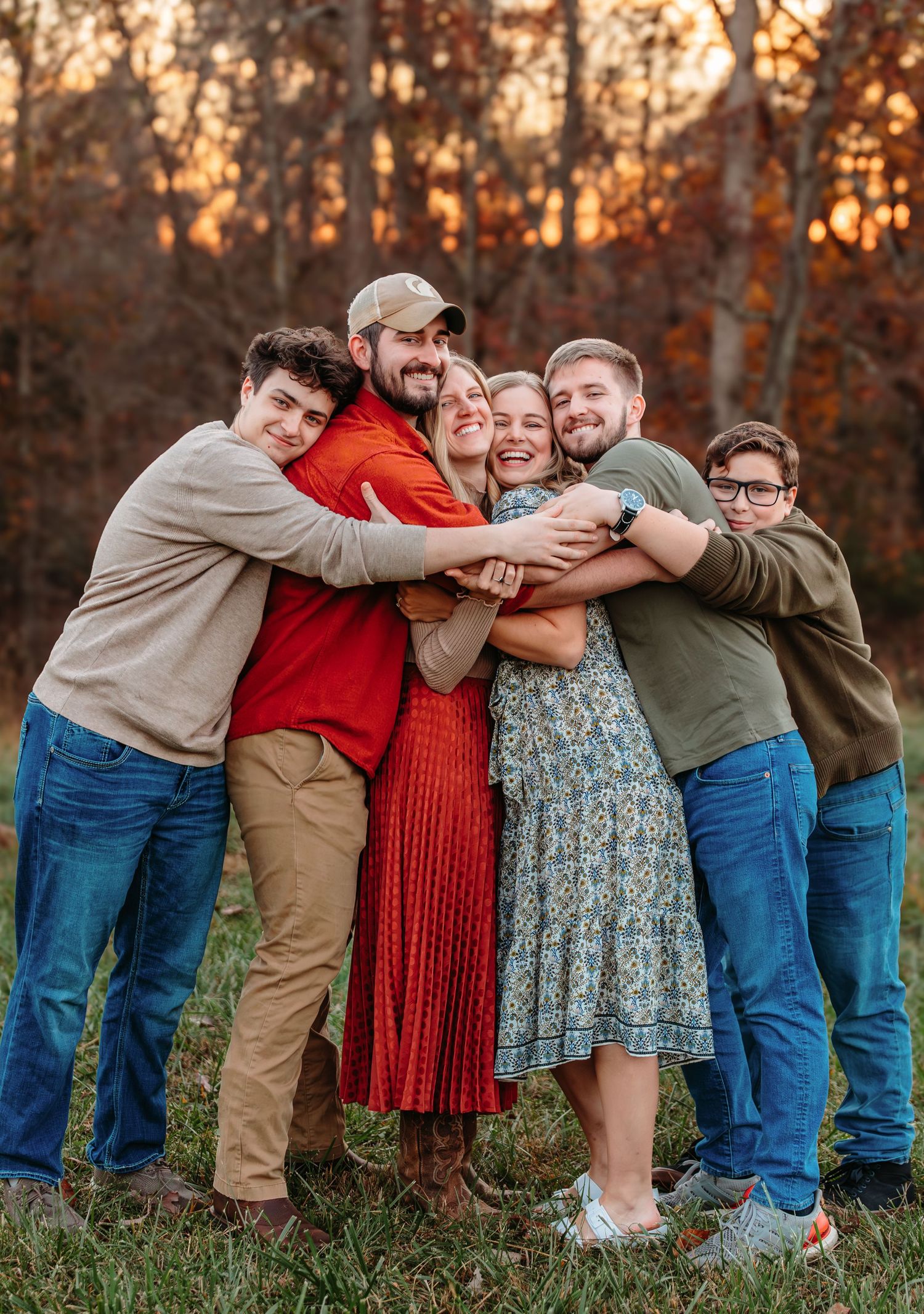 A group shares a warm embrace outdoors during golden hour with autumn trees in the background.
