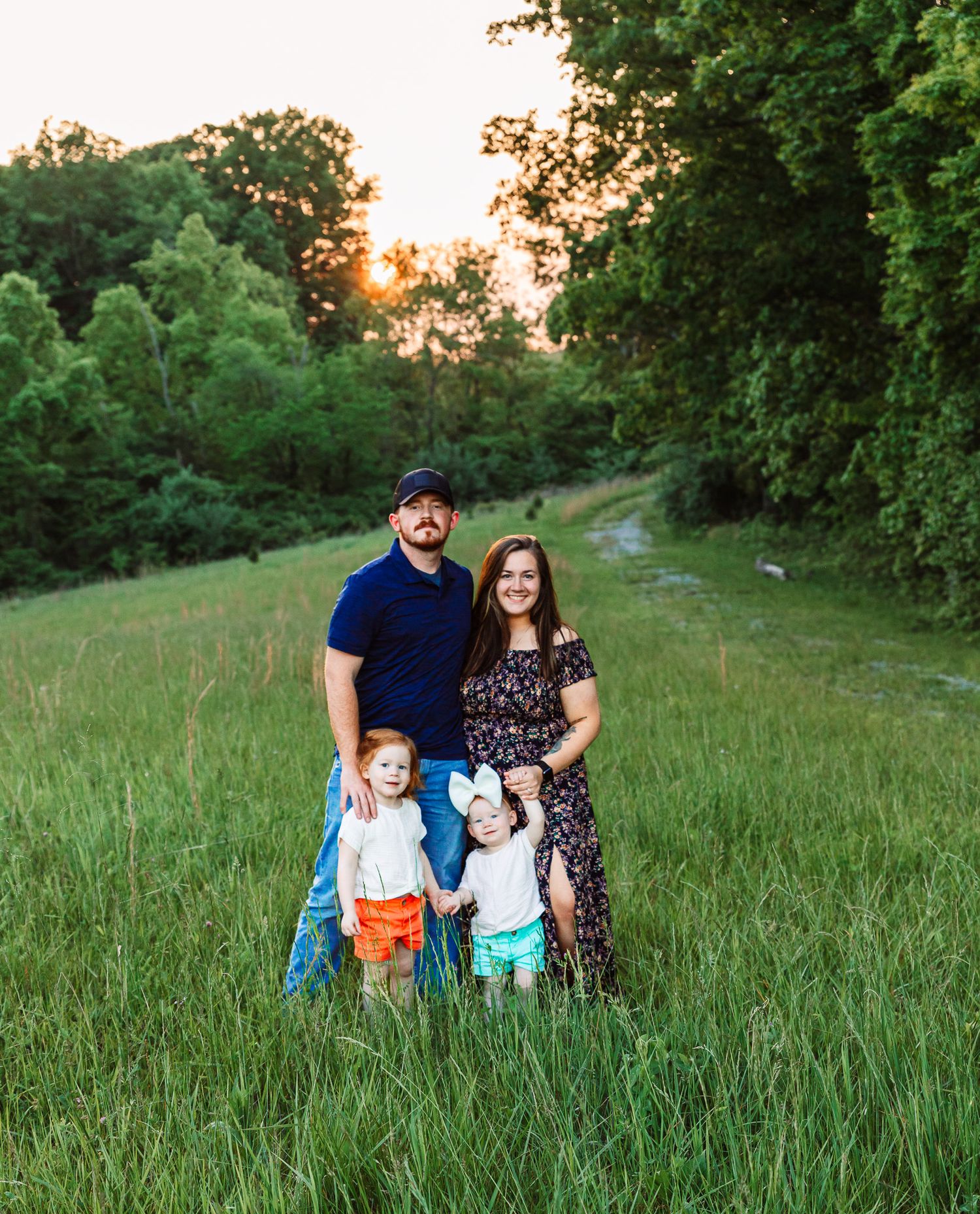 A family poses together in a lush green field during golden hour sunset.