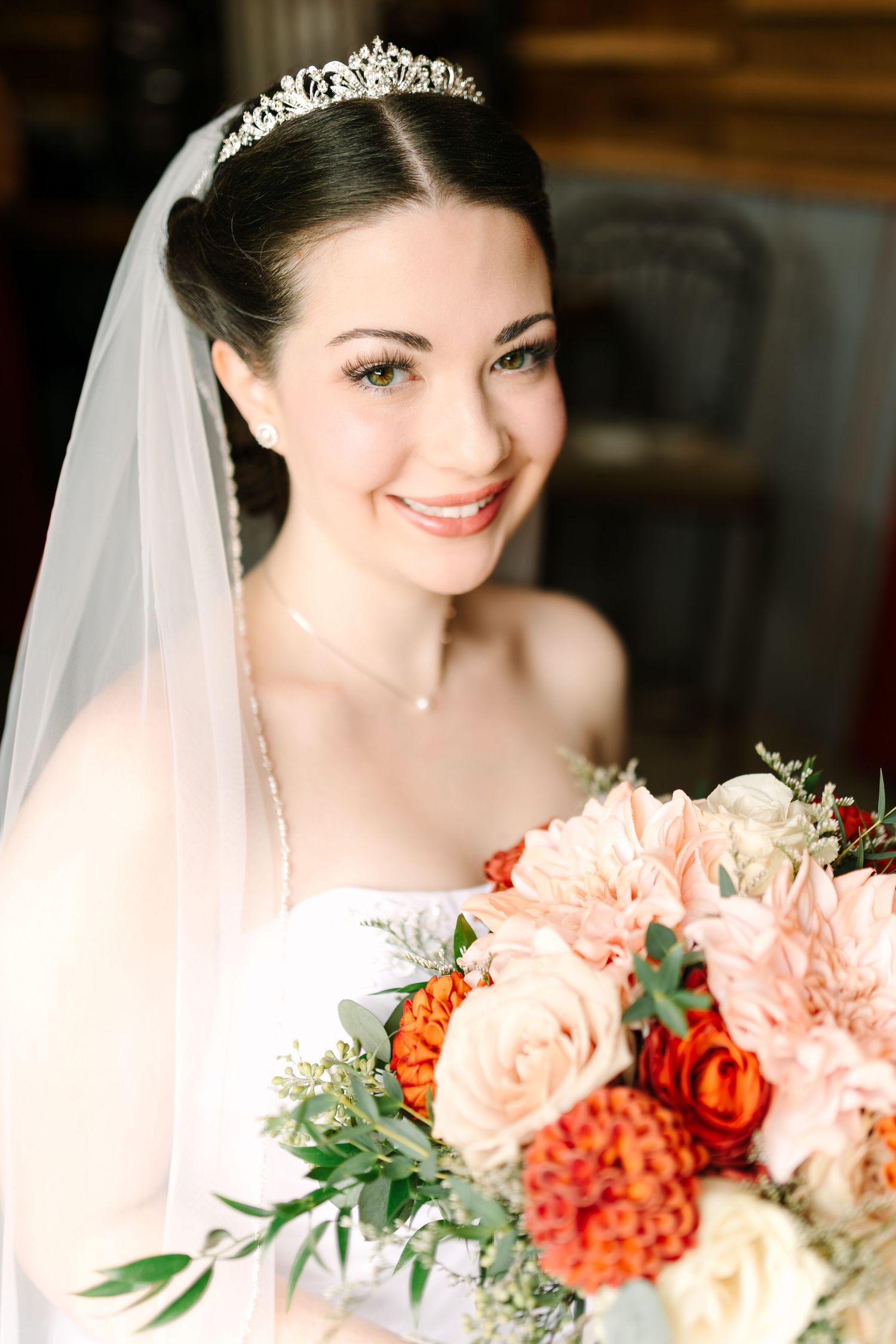 Close-up wedding photo showing a beautiful bride and a peach and coral bouquet with greenery and a flowing veil.