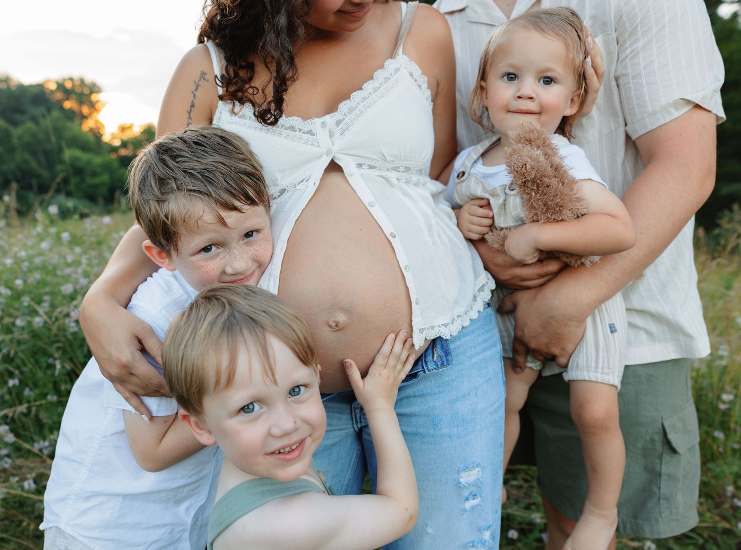 A candid family moment outdoors with a pregnant woman in white and young children.