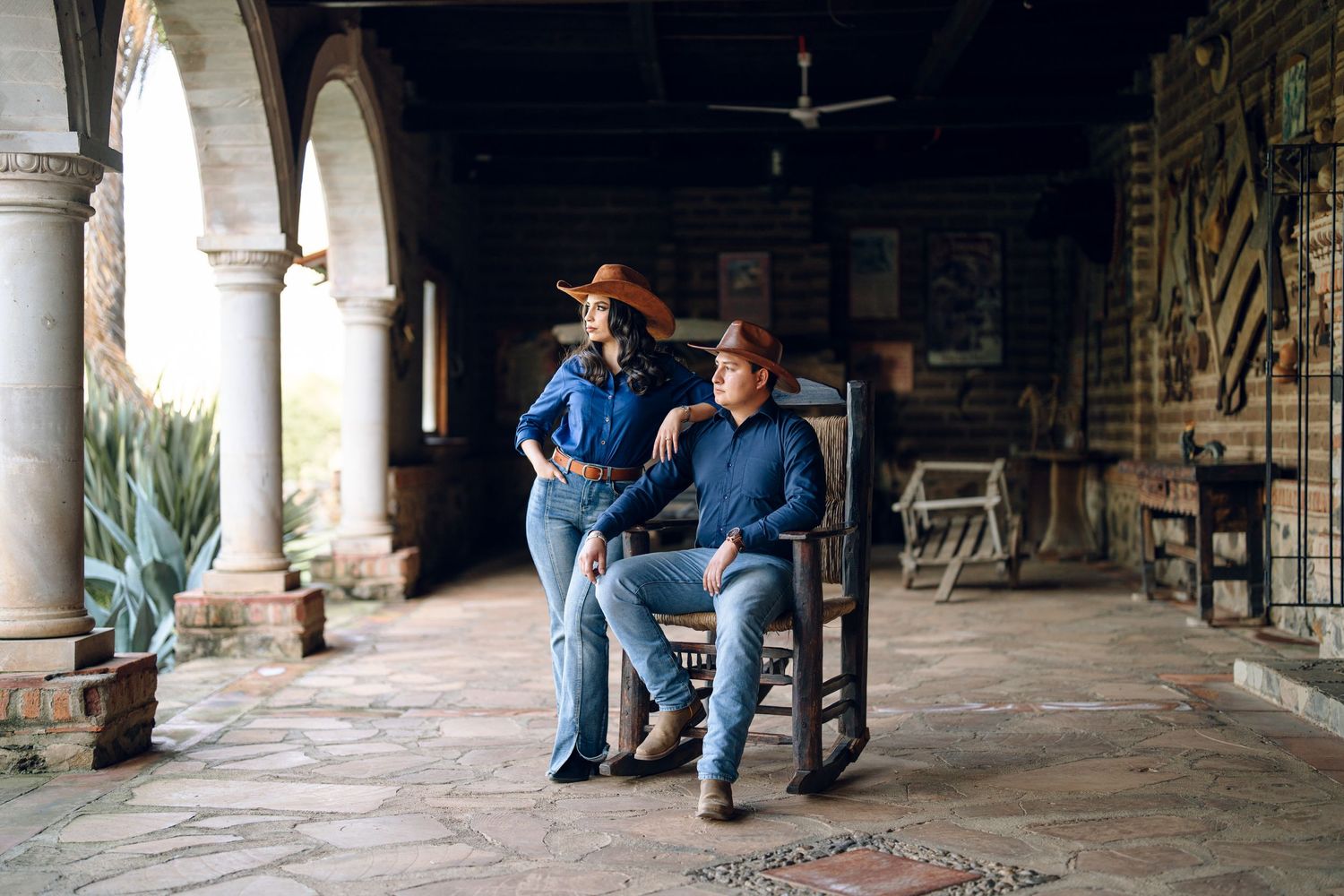 Rustic porch setting with stone columns creates dramatic shadows for engagement photos.