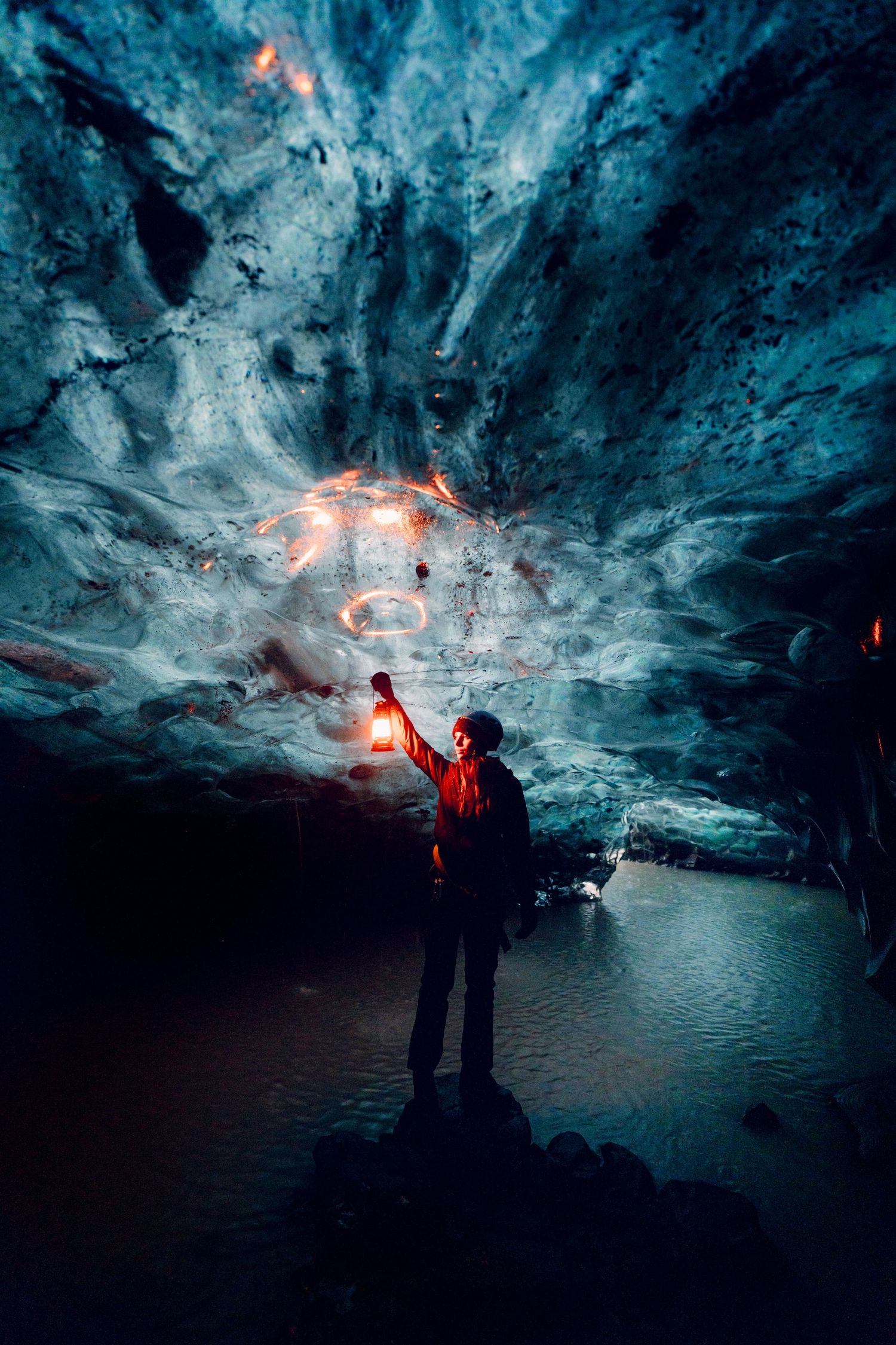 Explorer with red light illuminating dramatic blue ice cave interior.