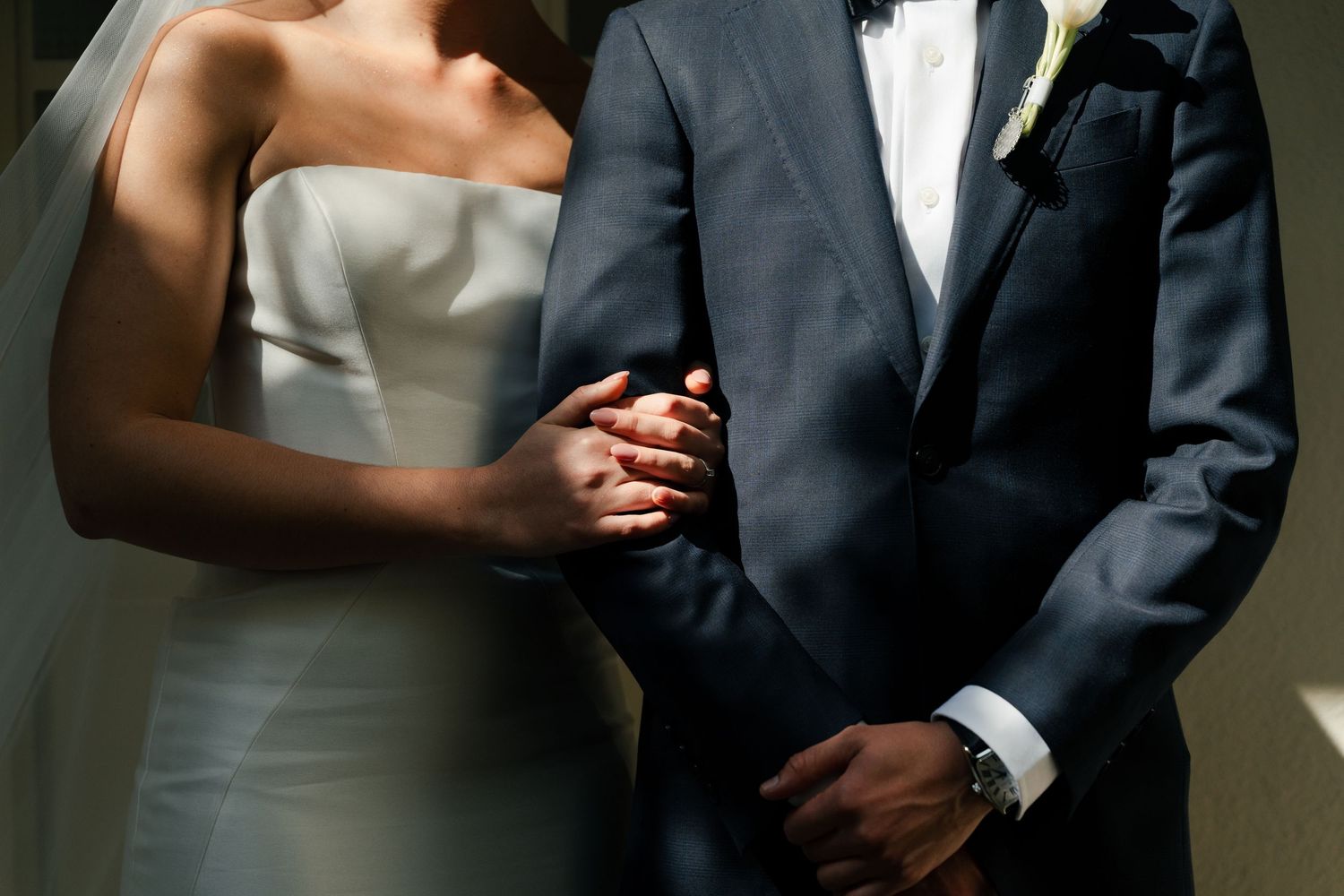 Bride in strapless white gown holding groom's arm in navy suit at wedding ceremony.
