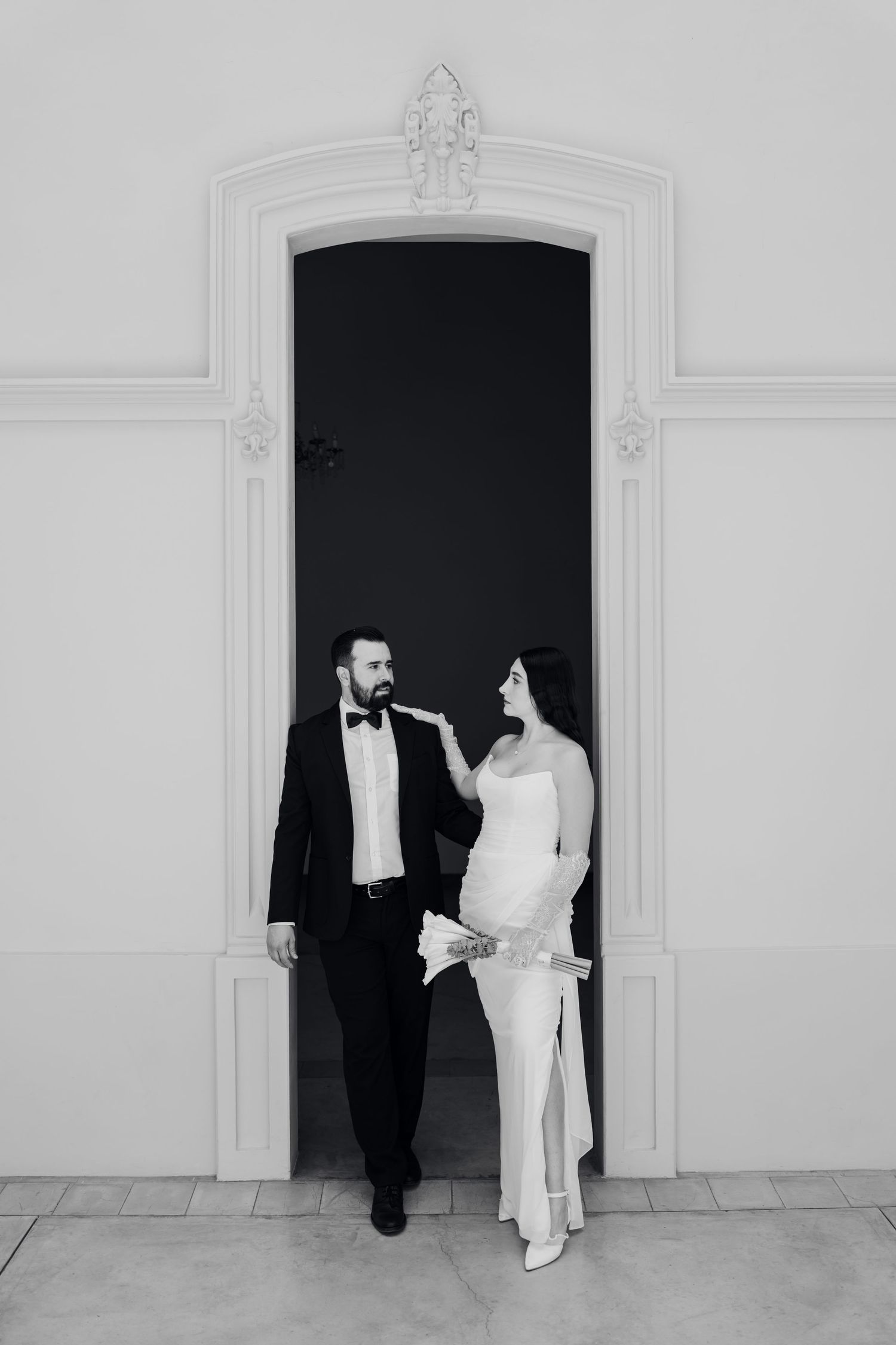 Black and white photo of elegant bride and groom posing in ornate arched doorway during wedding portrait session.