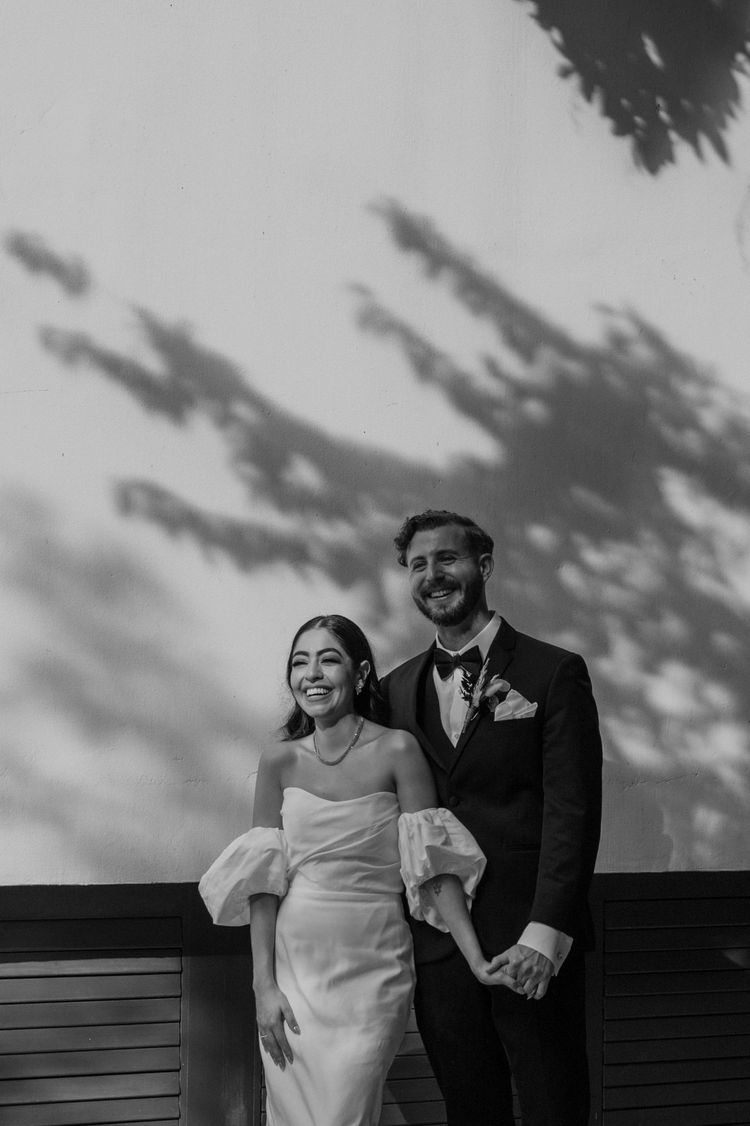 Elegant black and white portrait of newlyweds with dramatic tree shadow patterns.