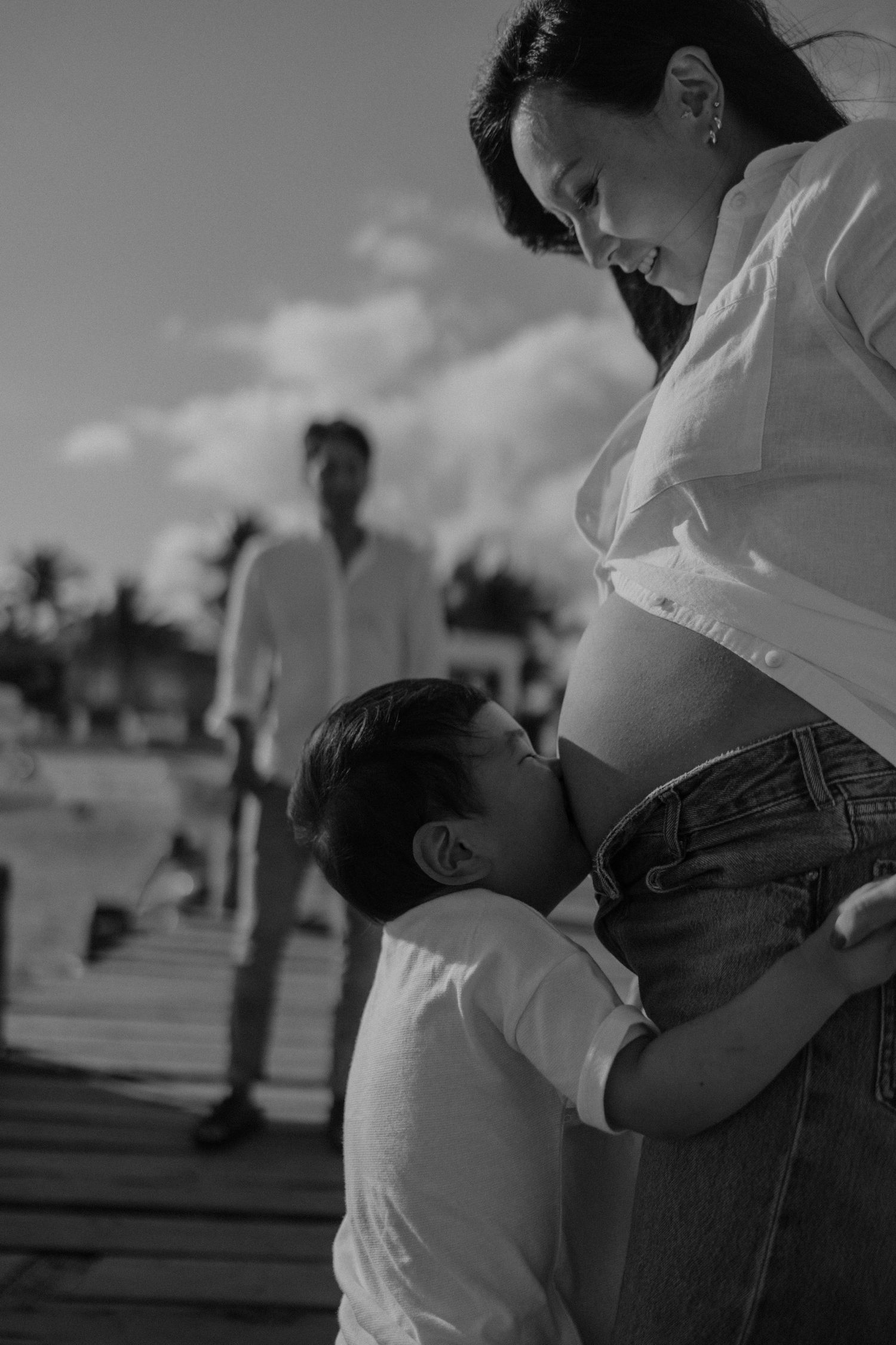 Black and white photo showing a tender moment between family members on a wooden boardwalk in Puerto Morelos Mexico.