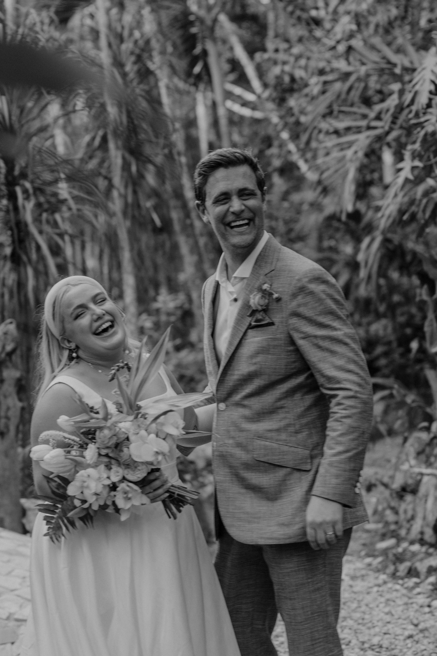 Black and white candid photo of newlyweds laughing together in a garden setting.