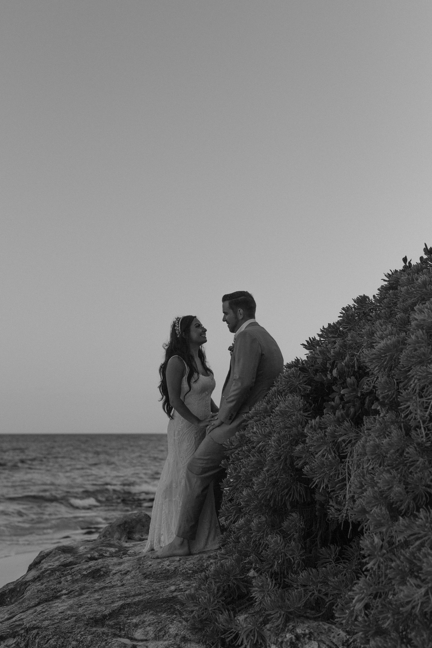 Silhouetted couple in wedding attire standing on coastal cliffs at dusk.