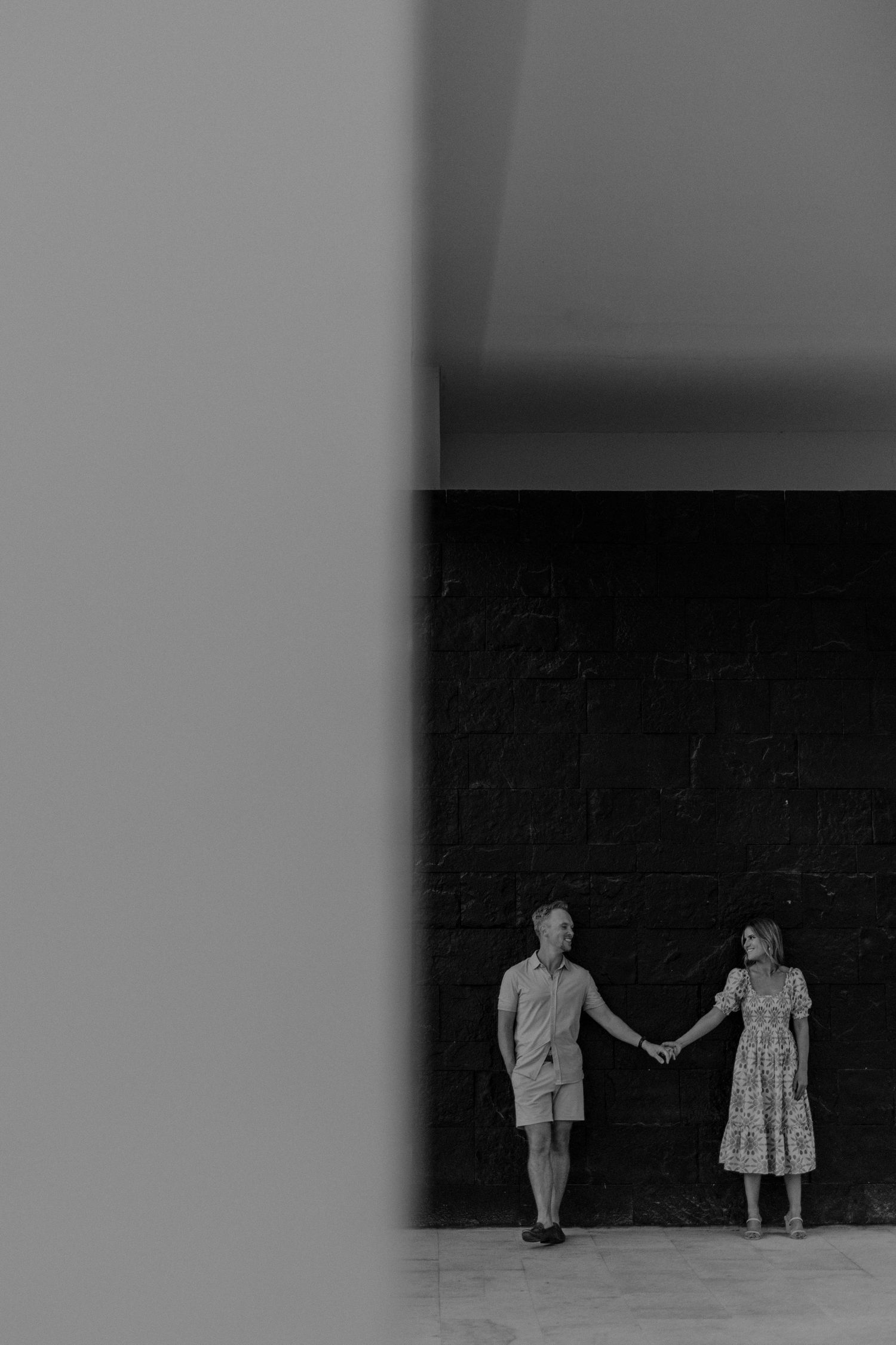 Editorial engagement portrait with couple holding hands in modern architectural setting in Riviera Maya.