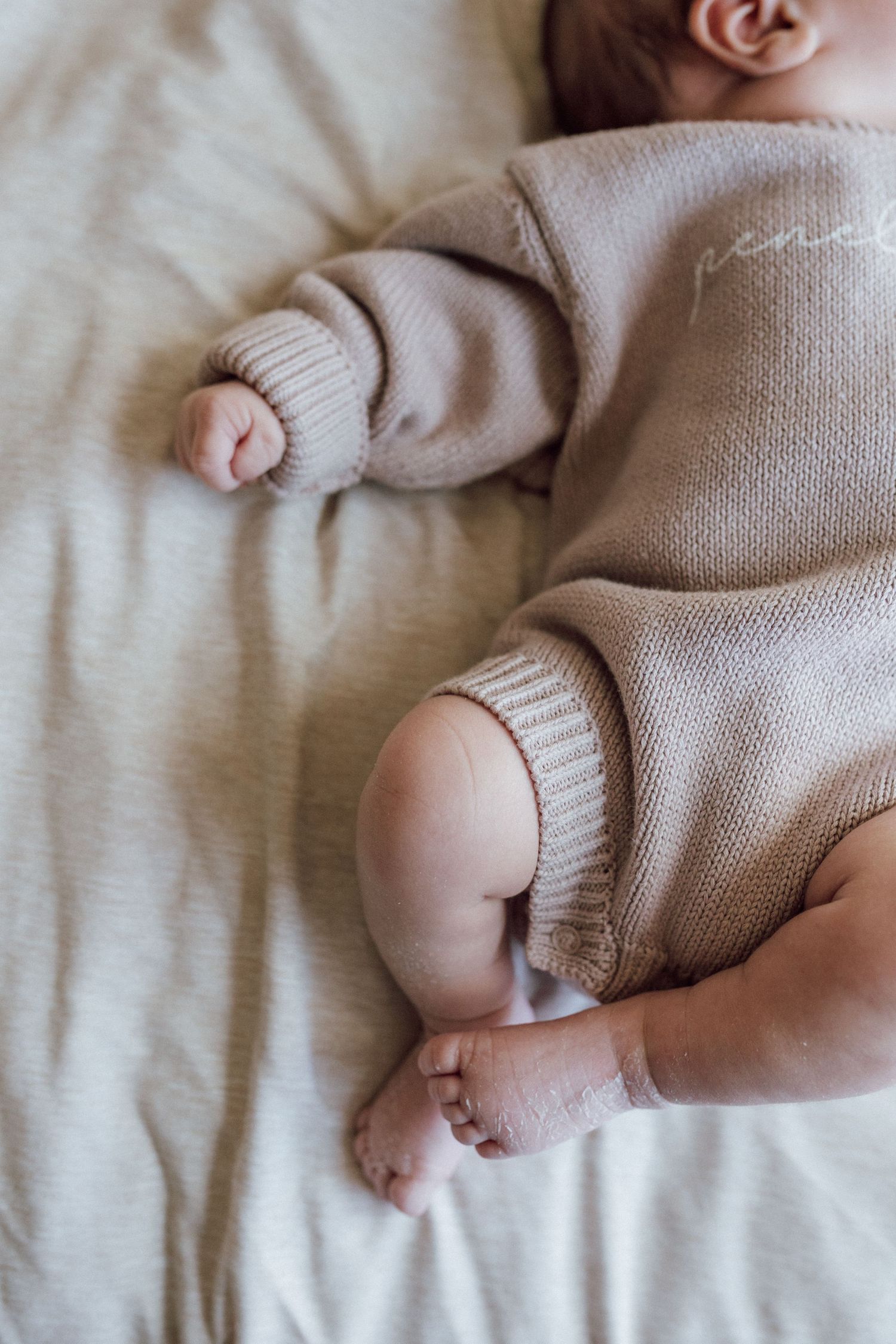 baby laying on bed in sweater outfit in home newborn photos