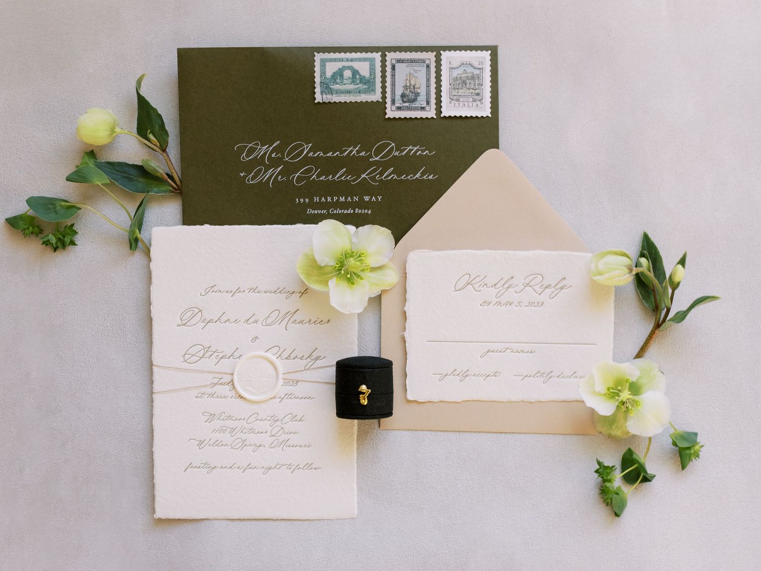 Elegant wedding invitation suite with white envelopes and delicate green floral accents arranged on a light gray surface.