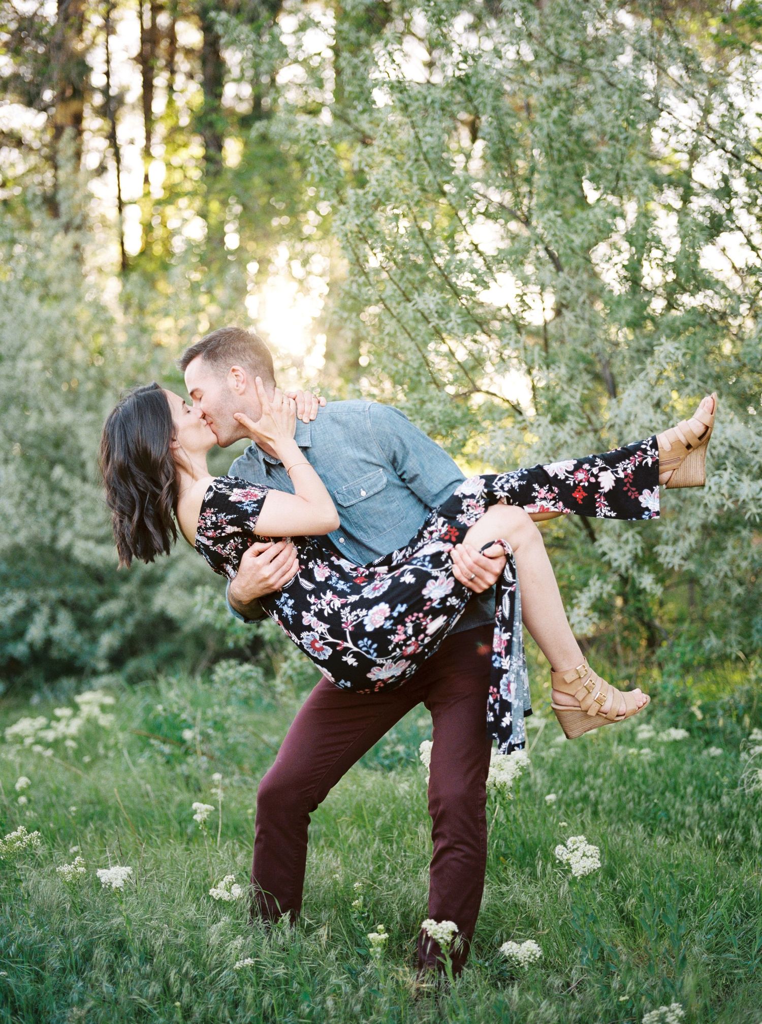 A romantic couple shares intimate dips and kisses in a sunlit forest setting surrounded by spring blossoms.